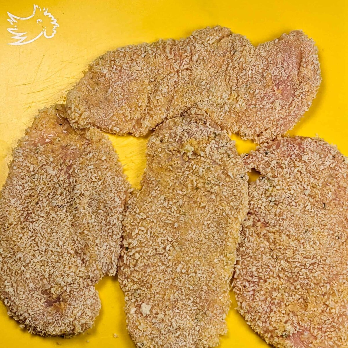 panko breaded chicken cutlets on a yellow cutting board mat.
