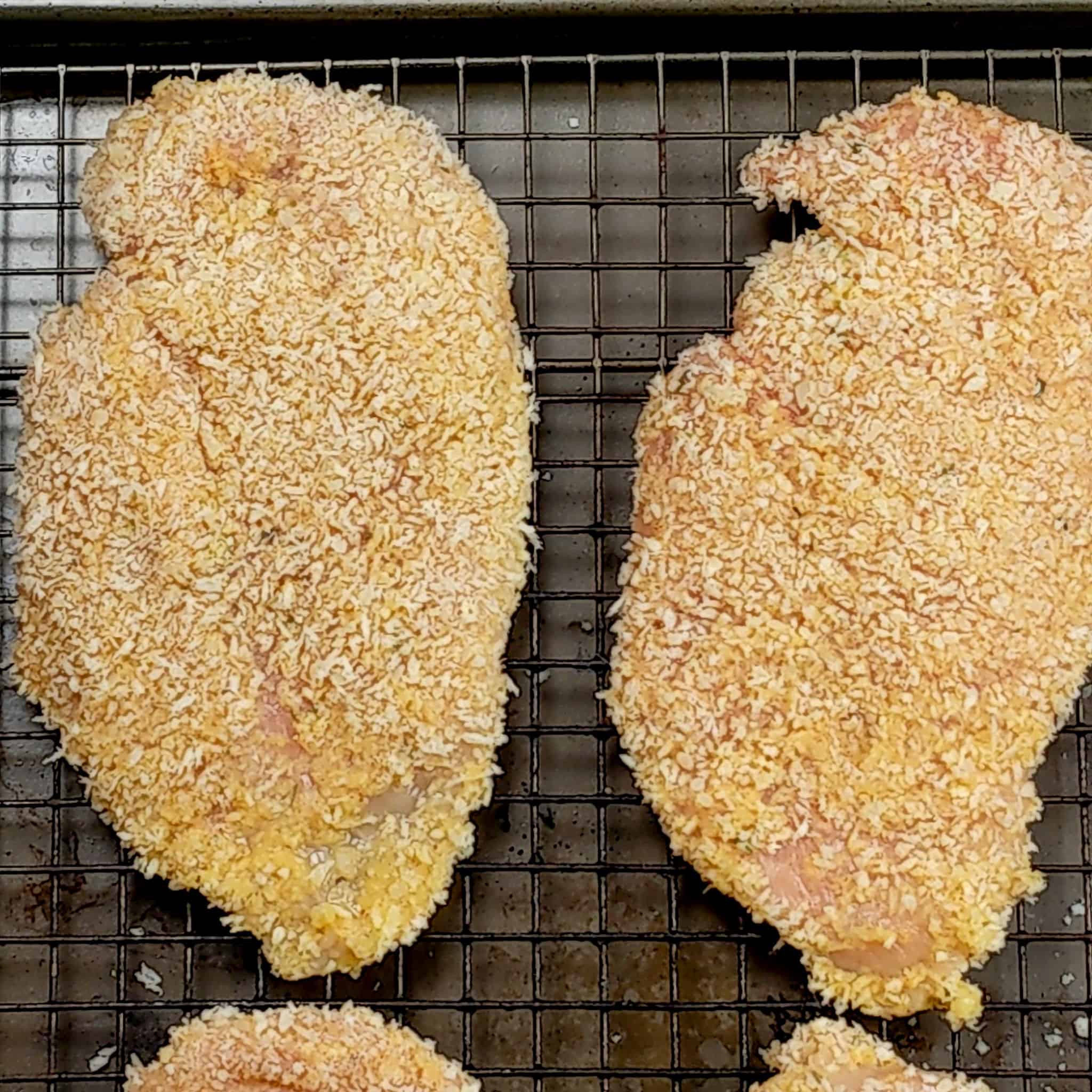 raw panko breaded chicken cutlets laying on a sheet pan with a wire rack