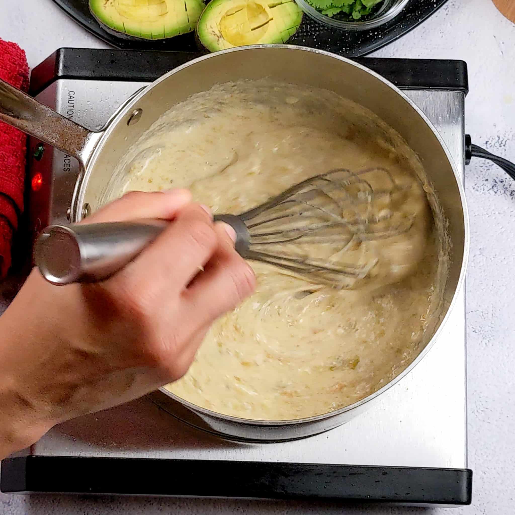 a large sauce pan with creamy salsa verde sauce being whisked on a stove top