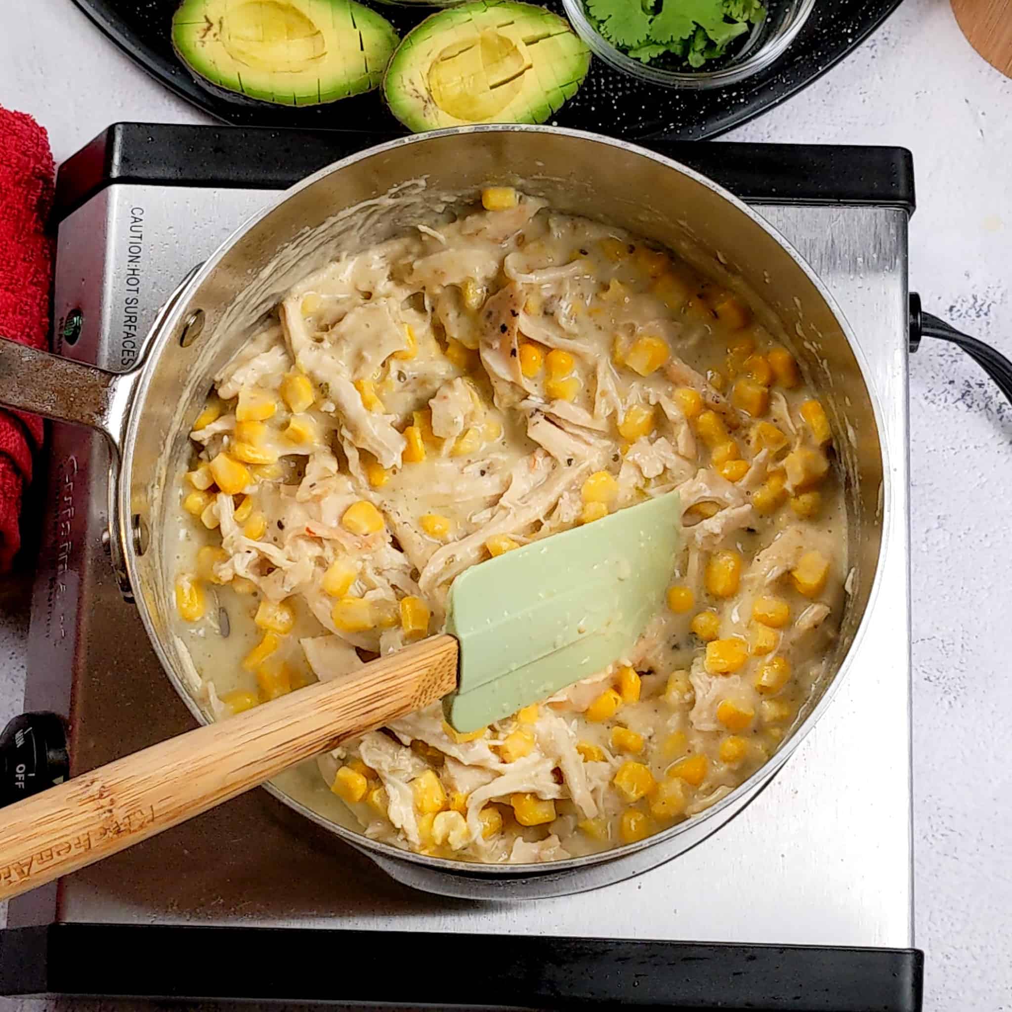 large saucepan with creamy salsa verde sauce, chicken kernels and shredded chicken combined with a silicone spatula sitting in it.
