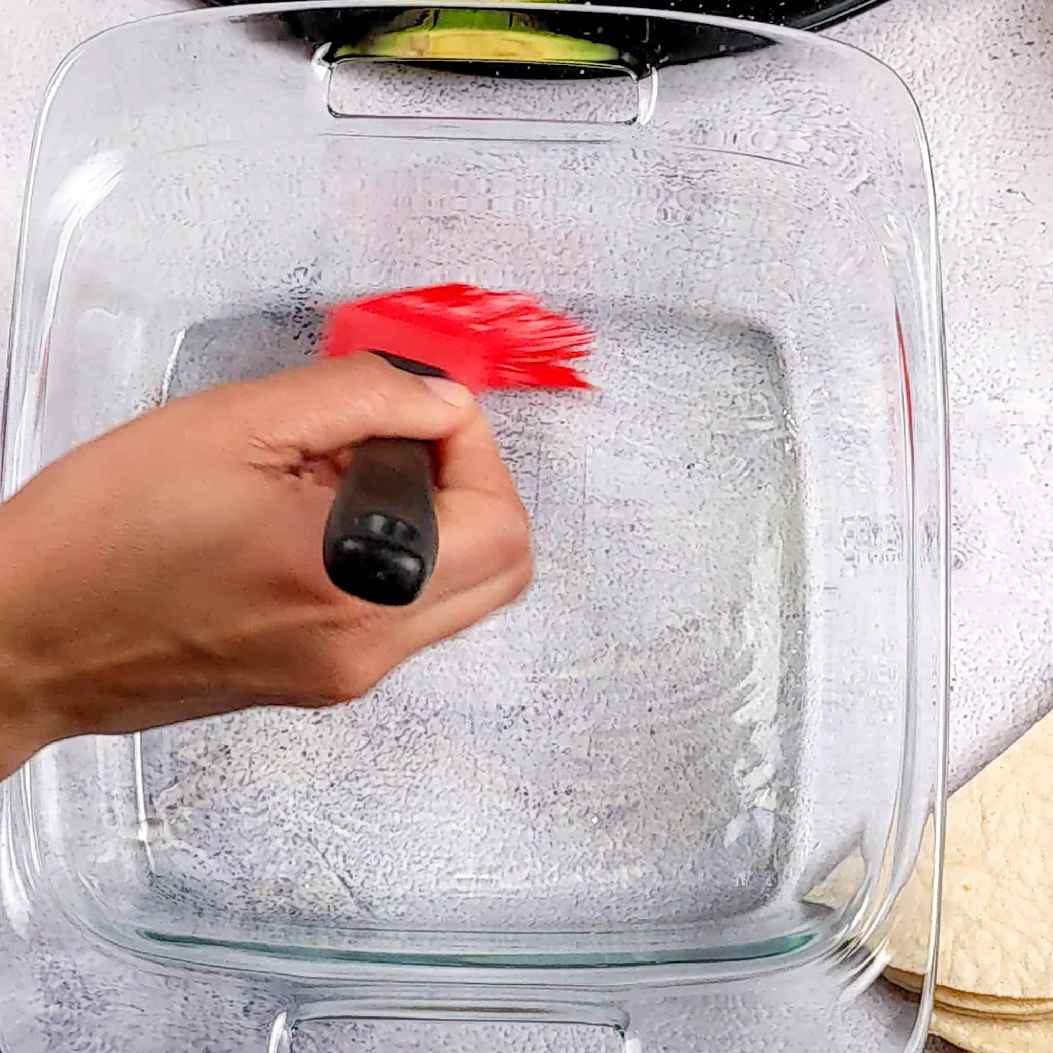 a square glass 8x8 baking dish being brushed with olive oil