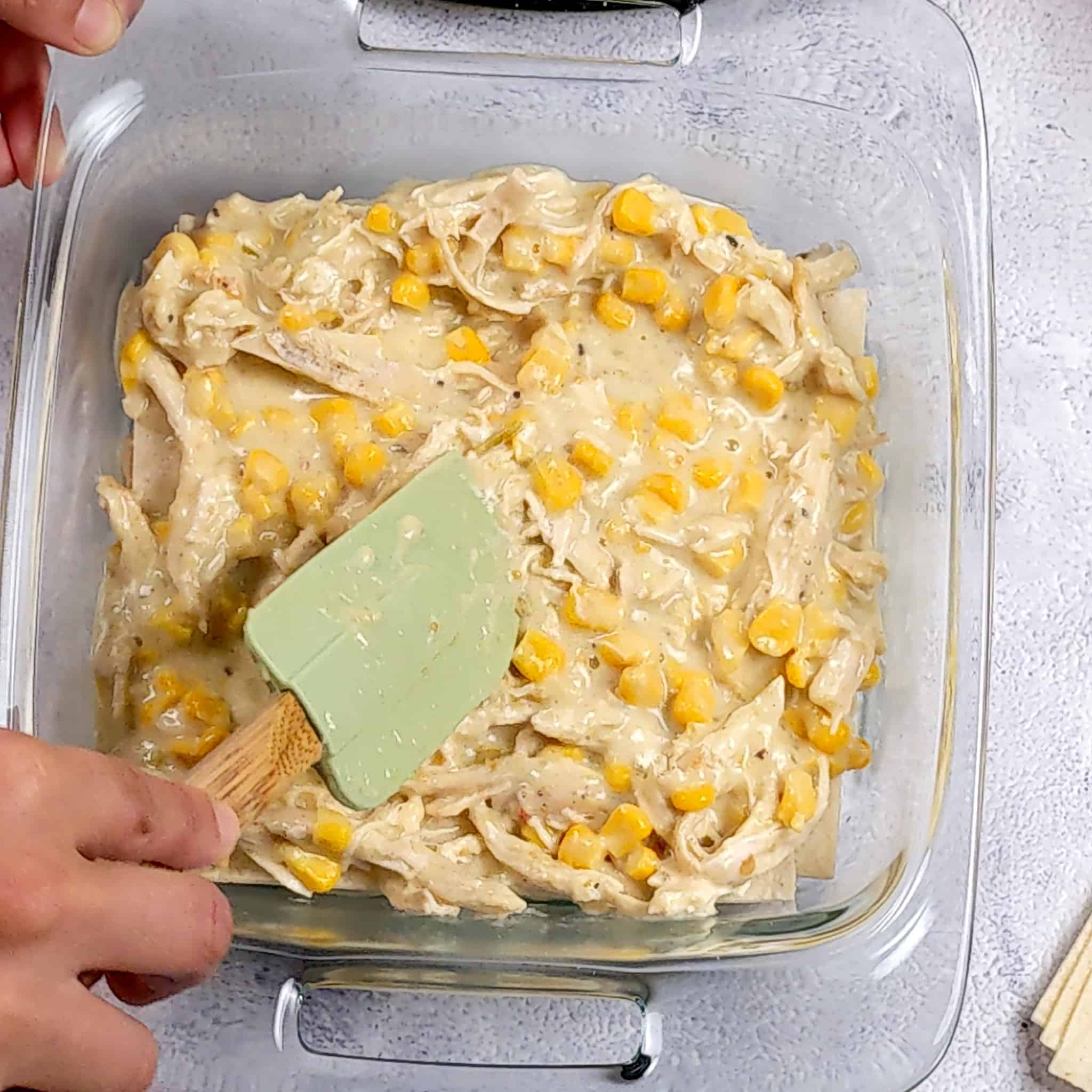 another layer of salsa verde chicken mixture being spread with a silicone spatula