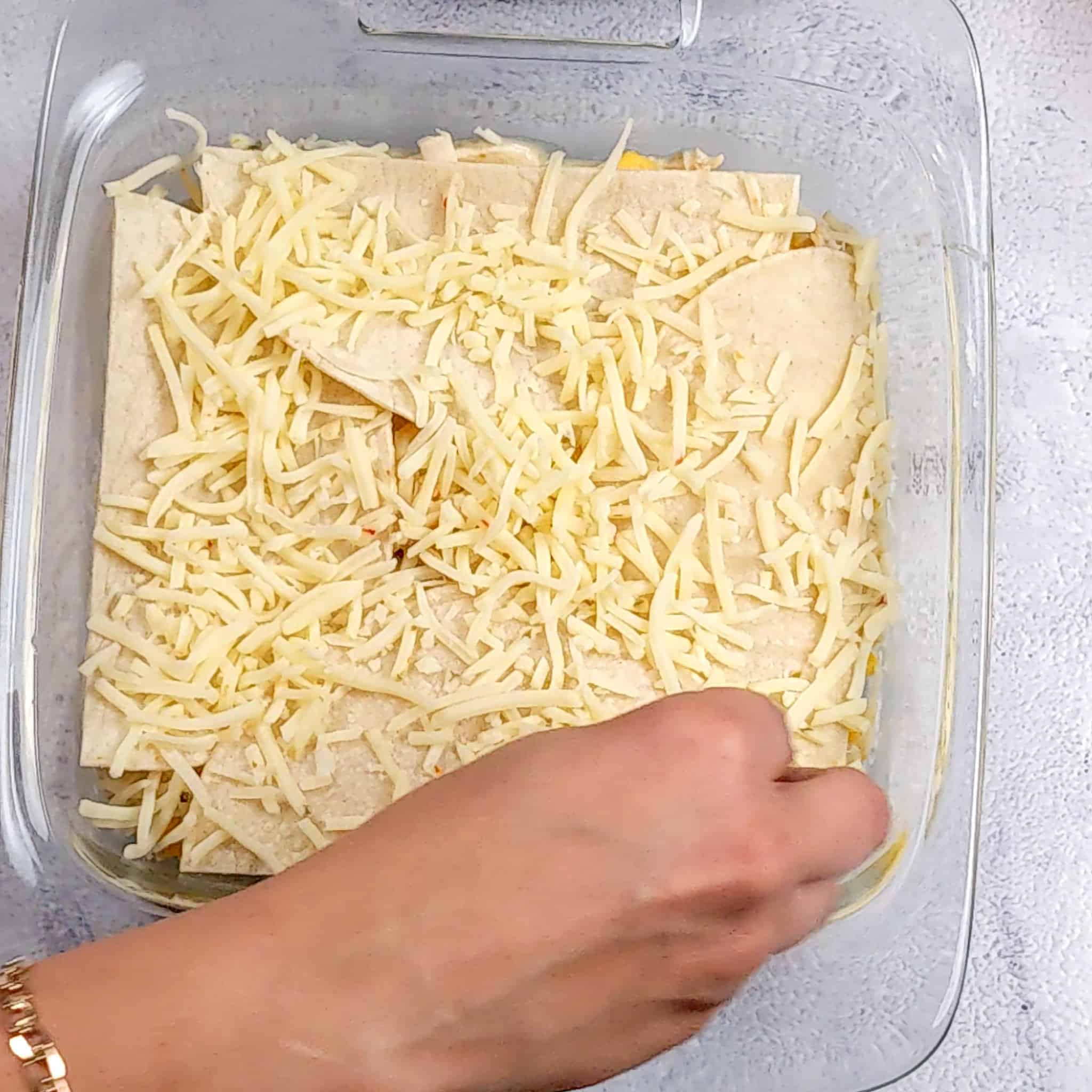 the final layer of halved corn tortillas being sprinkled with shredded cheese