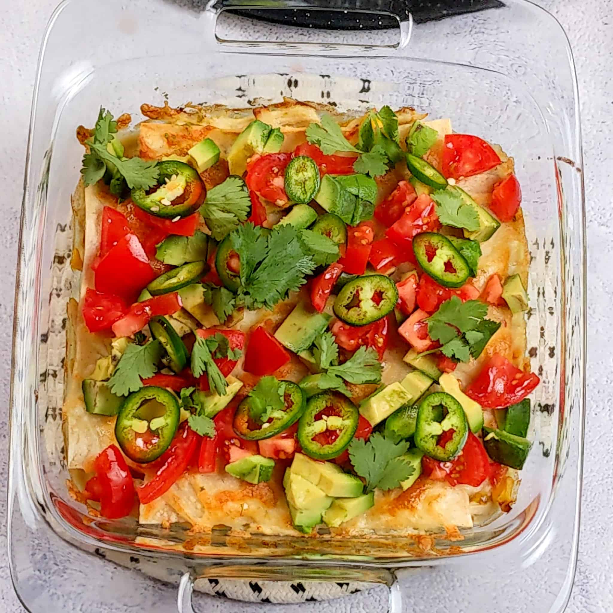 cilantro leaves, sliced jalapeno rings, diced tomatoes, and diced avocado pieces on top of the baked chicken tortilla casserole