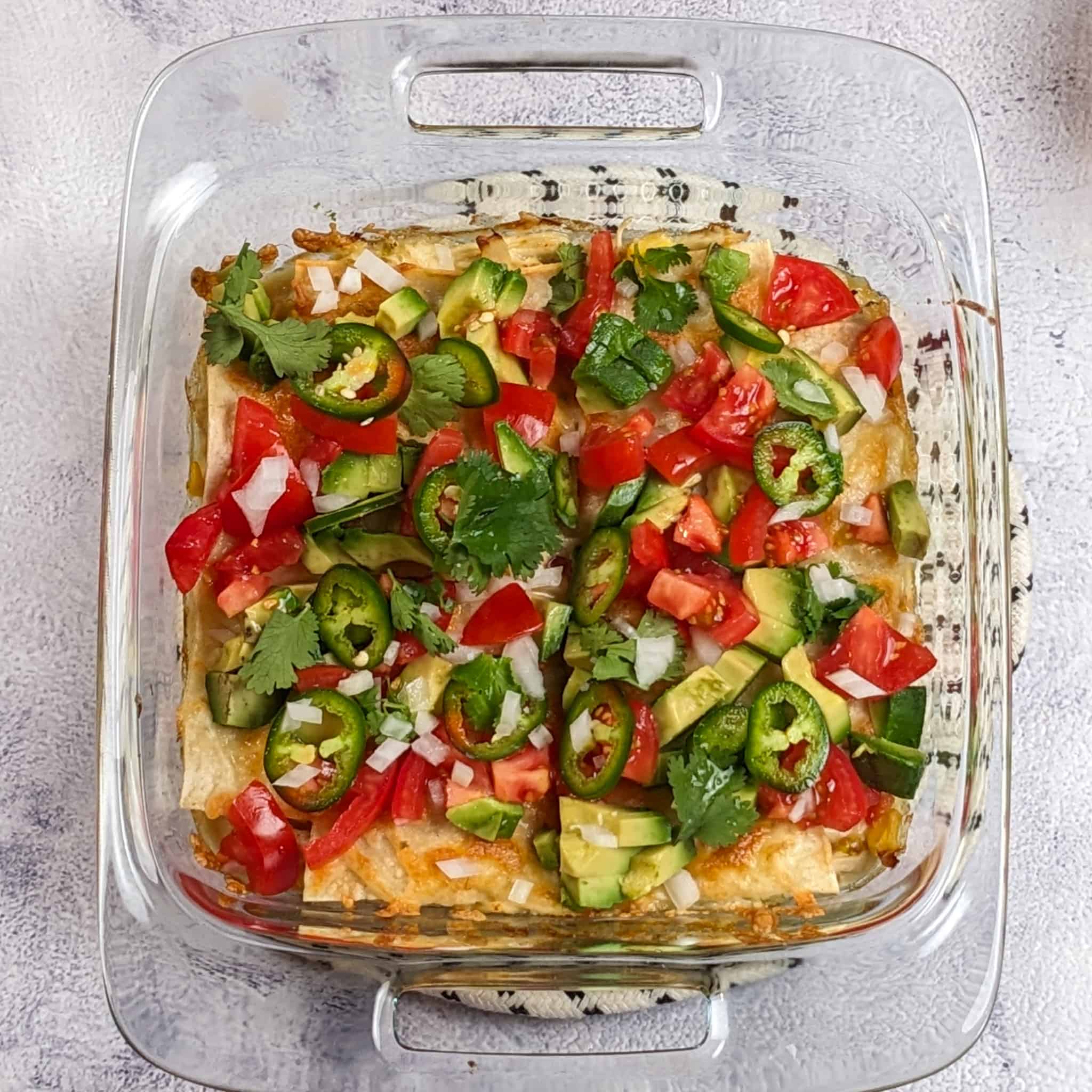 diced white onion, cilantro leaves, sliced jalapeno rings, diced tomatoes, and diced avocado pieces on top of the baked chicken tortilla casserole