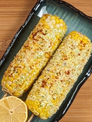 oven-baked parmesan pesto corn on the cob on a rectangular plate with half of a lemon on a wooden background