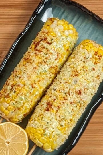 oven-baked parmesan pesto corn on the cob on a rectangular plate with half of a lemon on a wooden background