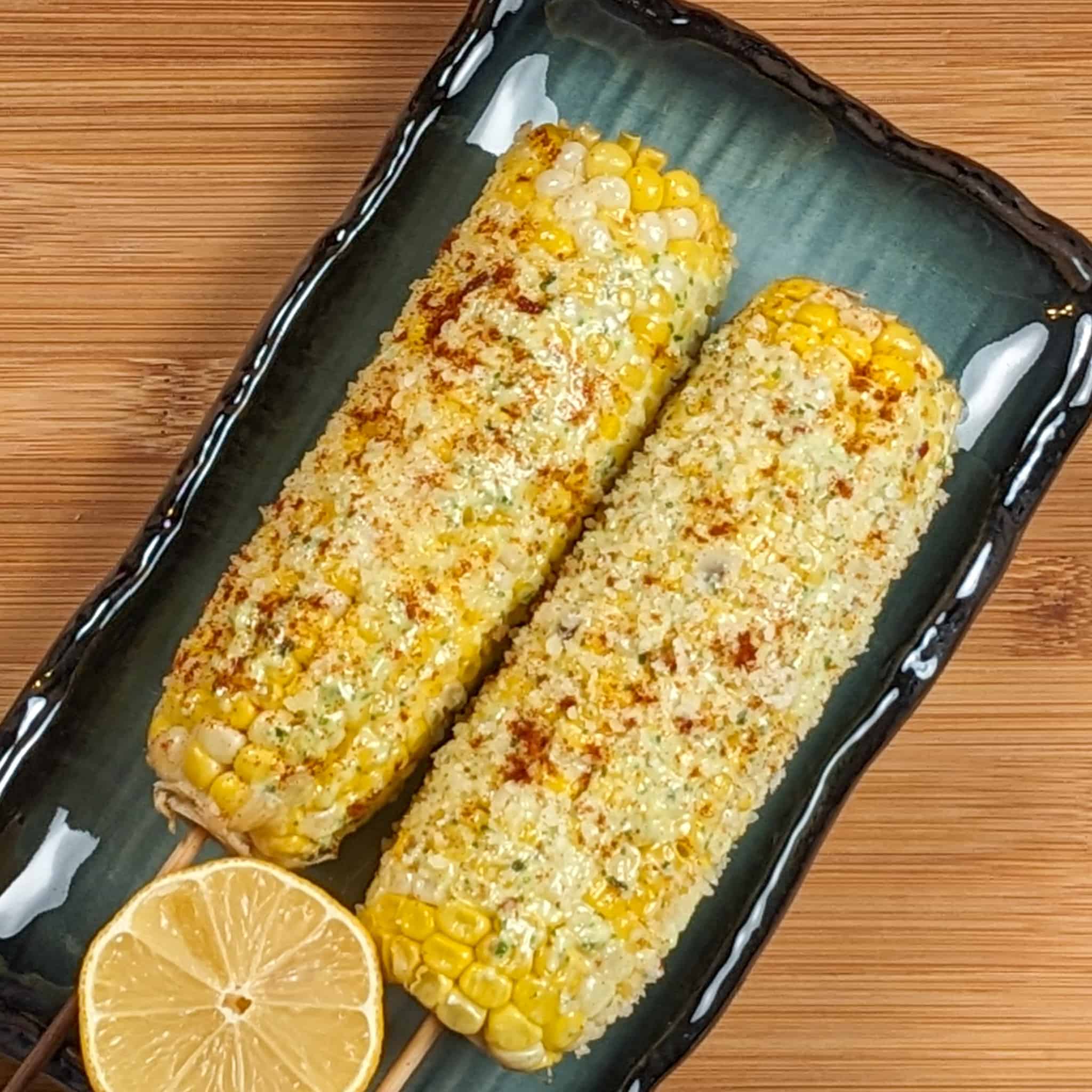 oven-baked parmesan pesto corn on the cob on a rectangular plate with half of a lemon on a wooden background