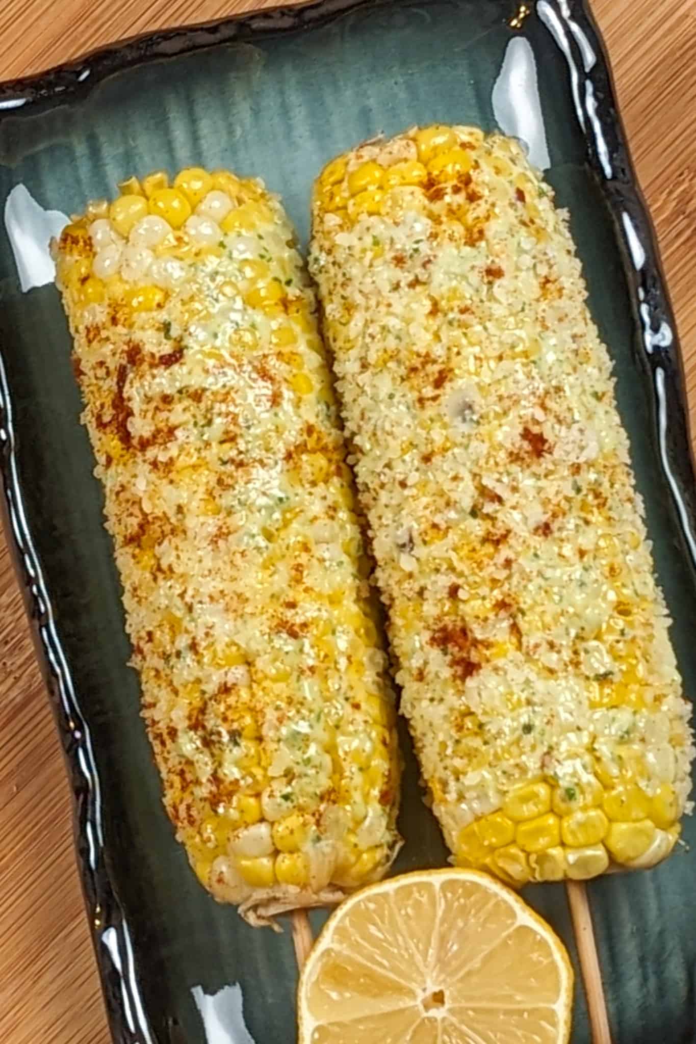 oven-baked parmesan pesto corn on the cob on a rectangular plate with half of a lemon on a wooden background