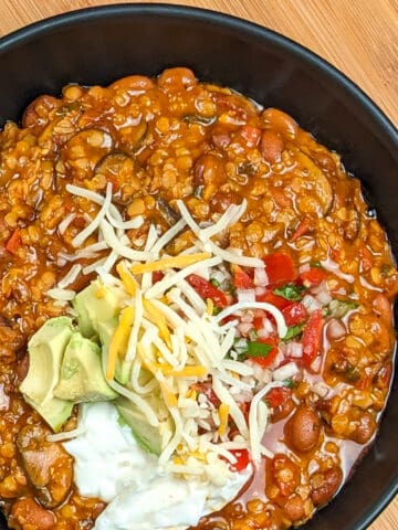 top view of Vegetarian Chipotle Mushroom Lentil Bean Chili in a wide soup bowl topped with sour cream, diced avocado, pico de gallo and pepper jack shredded cheese blend