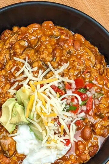 top view of Vegetarian Chipotle Mushroom Lentil Bean Chili in a wide soup bowl topped with sour cream, diced avocado, pico de gallo and pepper jack shredded cheese blend