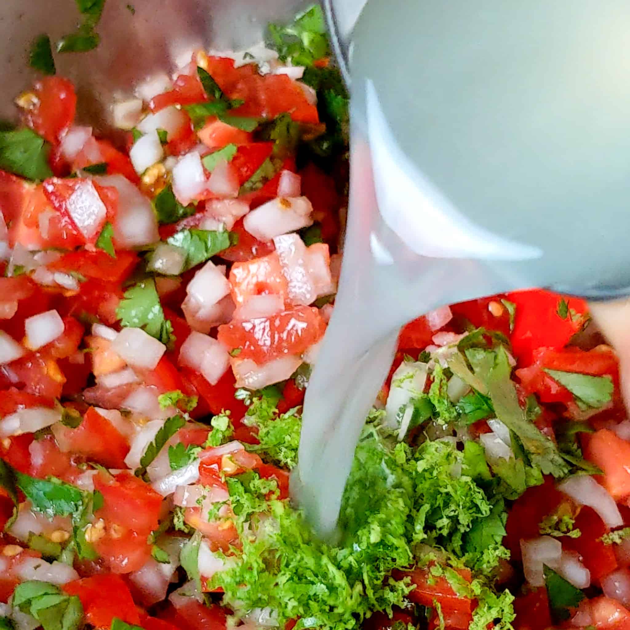 lime juice and lime zest added to a bowl of pico de gallo