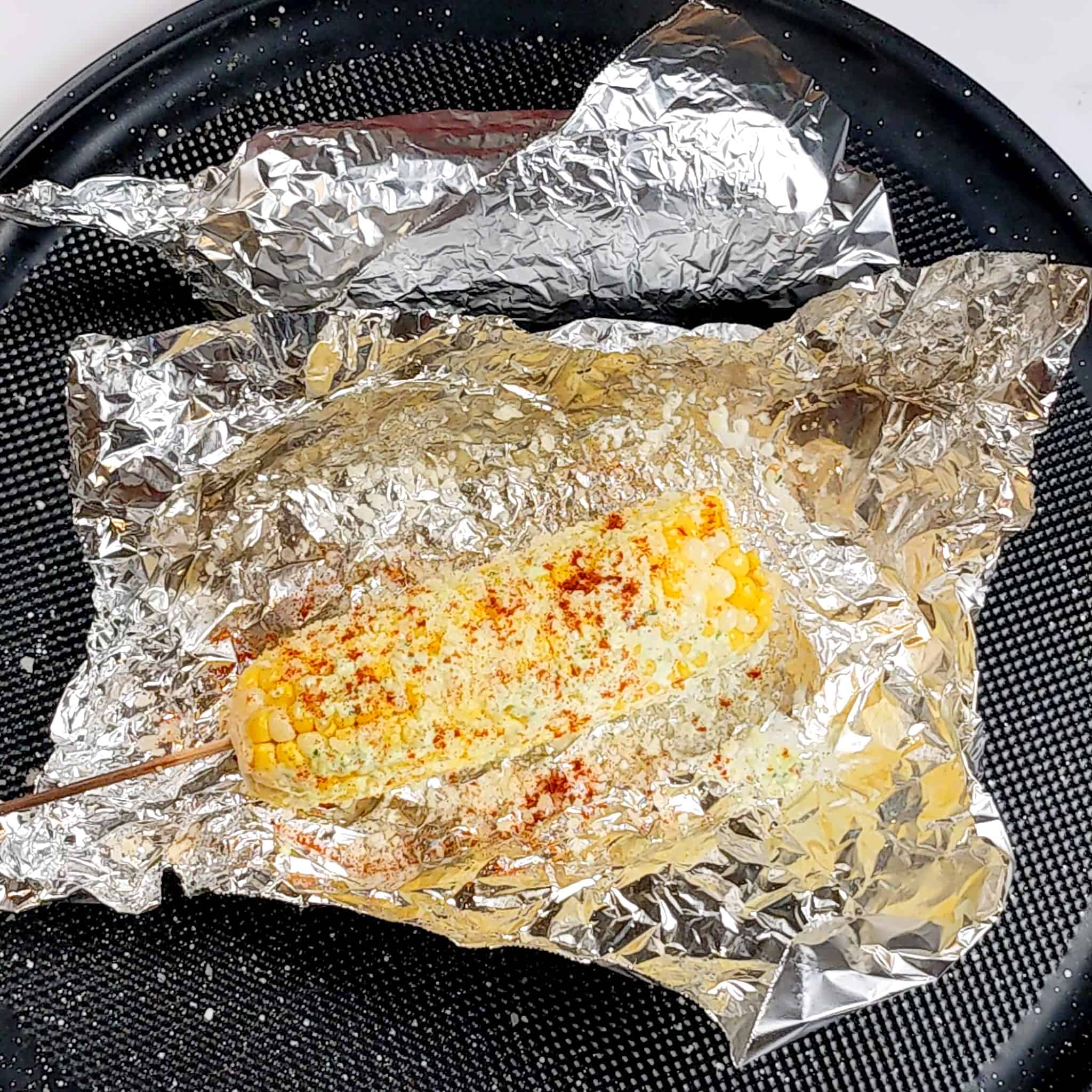 baked corn with pesto mayo and sprinkled with grated parmesan cheese and smoked paprika in foil on a round