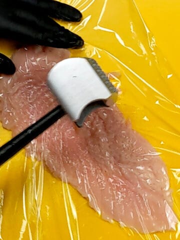 halved chicken being pounded out with a meat mallet on a yellow cutting board