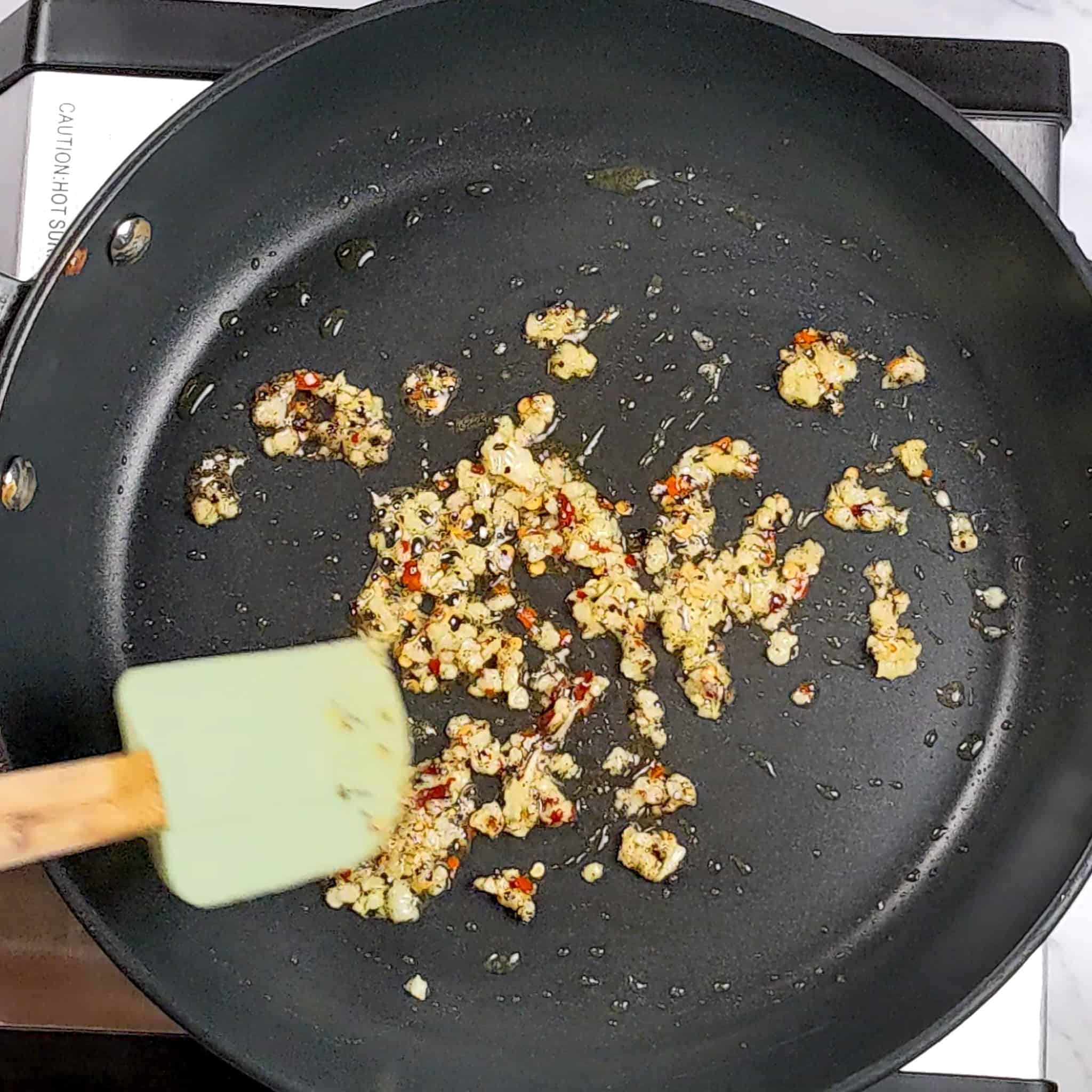 a nonstick frying pan with cooked minced garlic and red pepper chili flakes being stirred with a silicone spatula