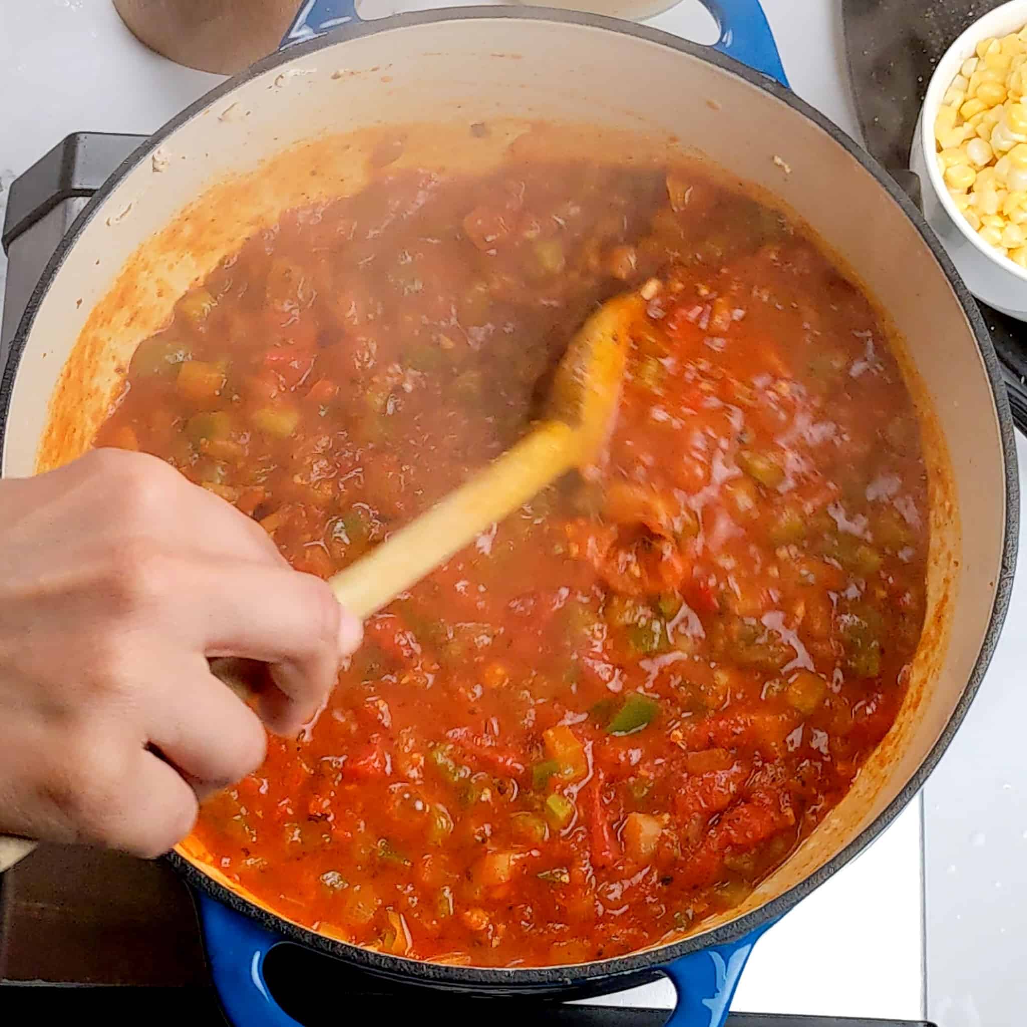 the broken down cooked tomato mixture being stirred with a wooden spoon