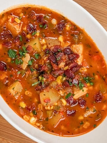 top view of the spicy calabrian pepper tomato chicken chowder with chopped bacon and parsley in an oval wide bowl on a wooden counter