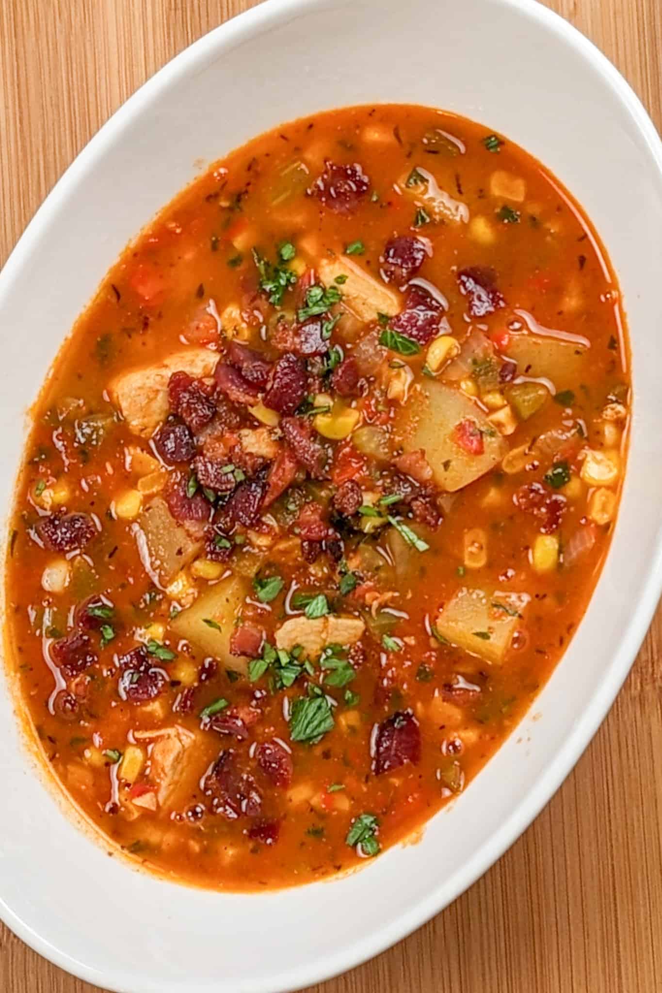 top view of the spicy calabrian pepper tomato chicken chowder with chopped bacon and parsley in an oval wide bowl on a wooden counter