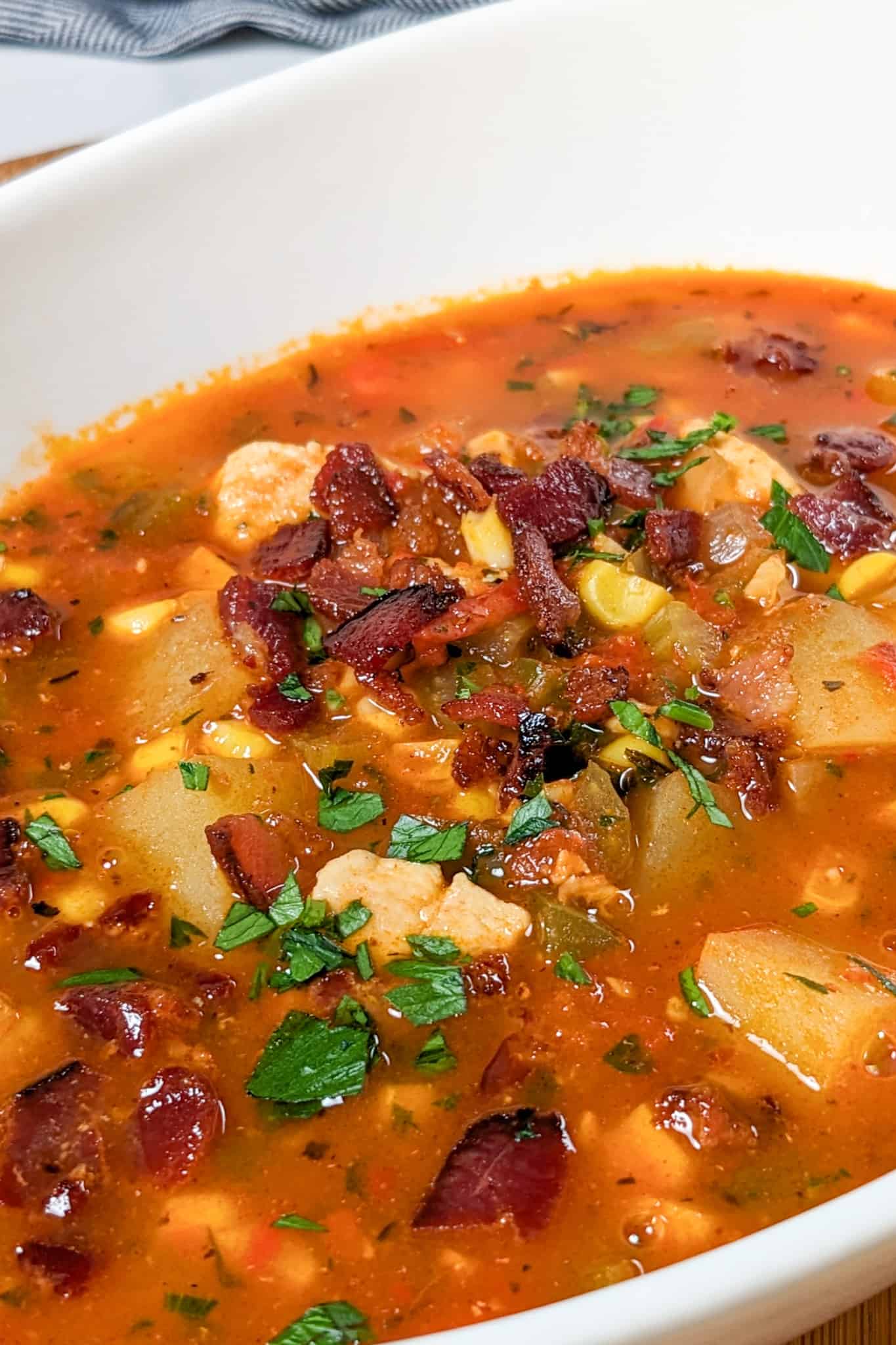 side view of the spicy calabrian pepper tomato chicken chowder with chopped bacon and parsley in an oval wide bowl on a wooden counter