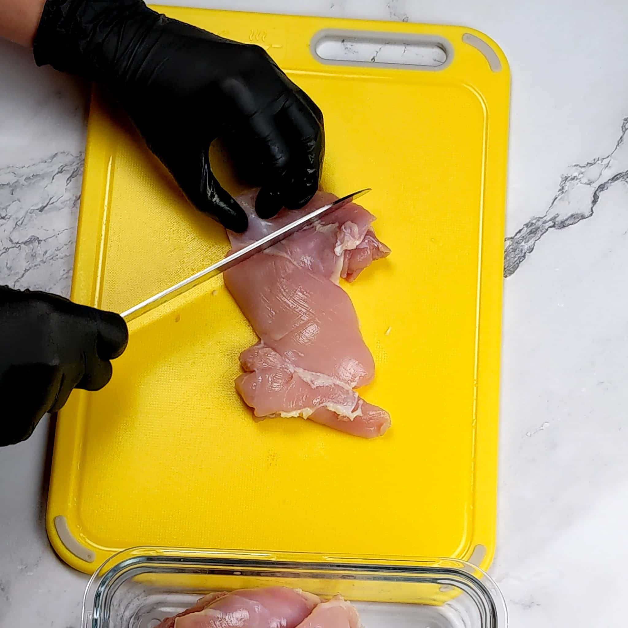 a chicken thigh being cut with a knife to create slits on a plastic cutting board.