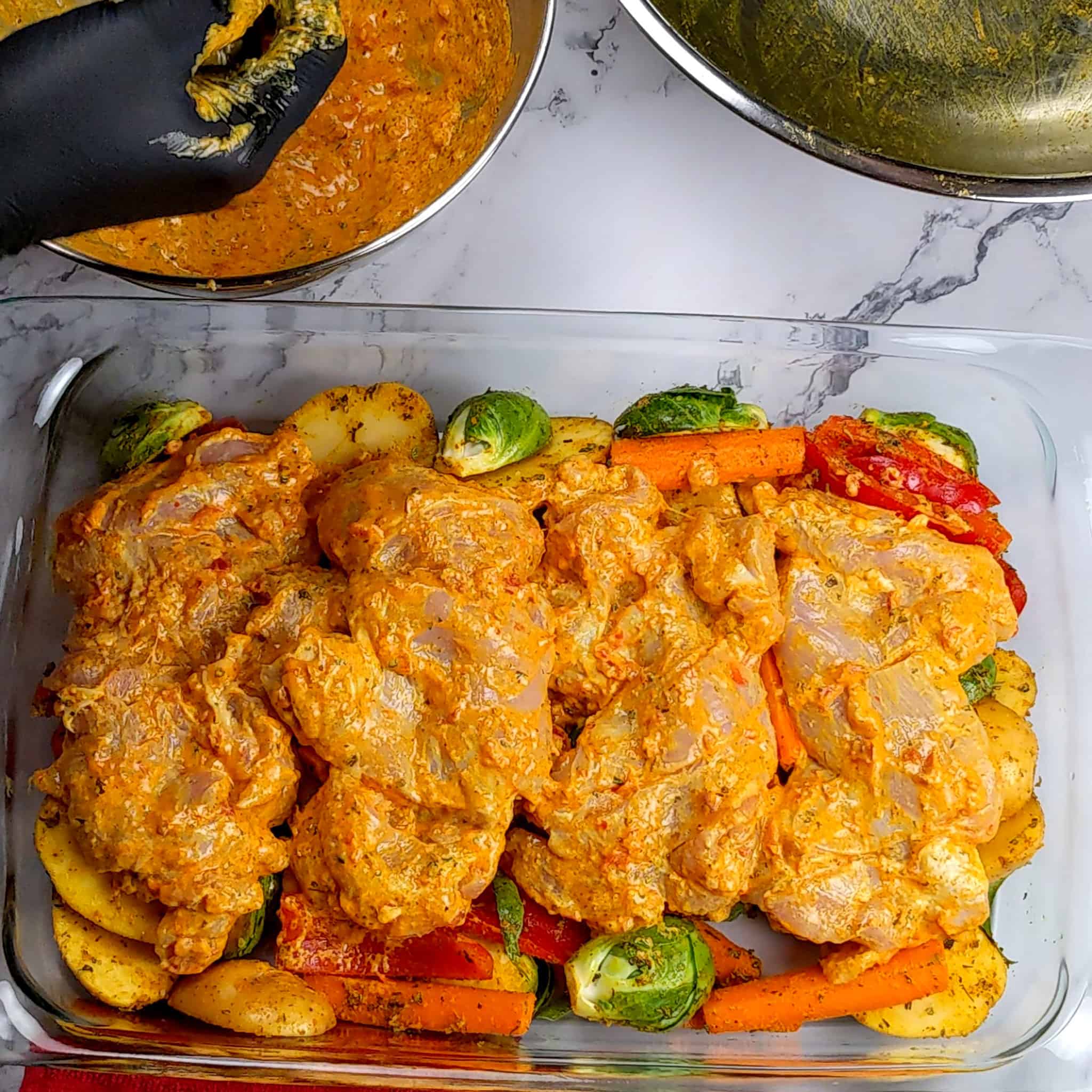 seasoned vegetables and yogurt marinated chicken thighs layered in a rectangle glass baking dish for the Calabrian Pepper & Lemon Yogurt Baked Chicken and Vegetables recipe.