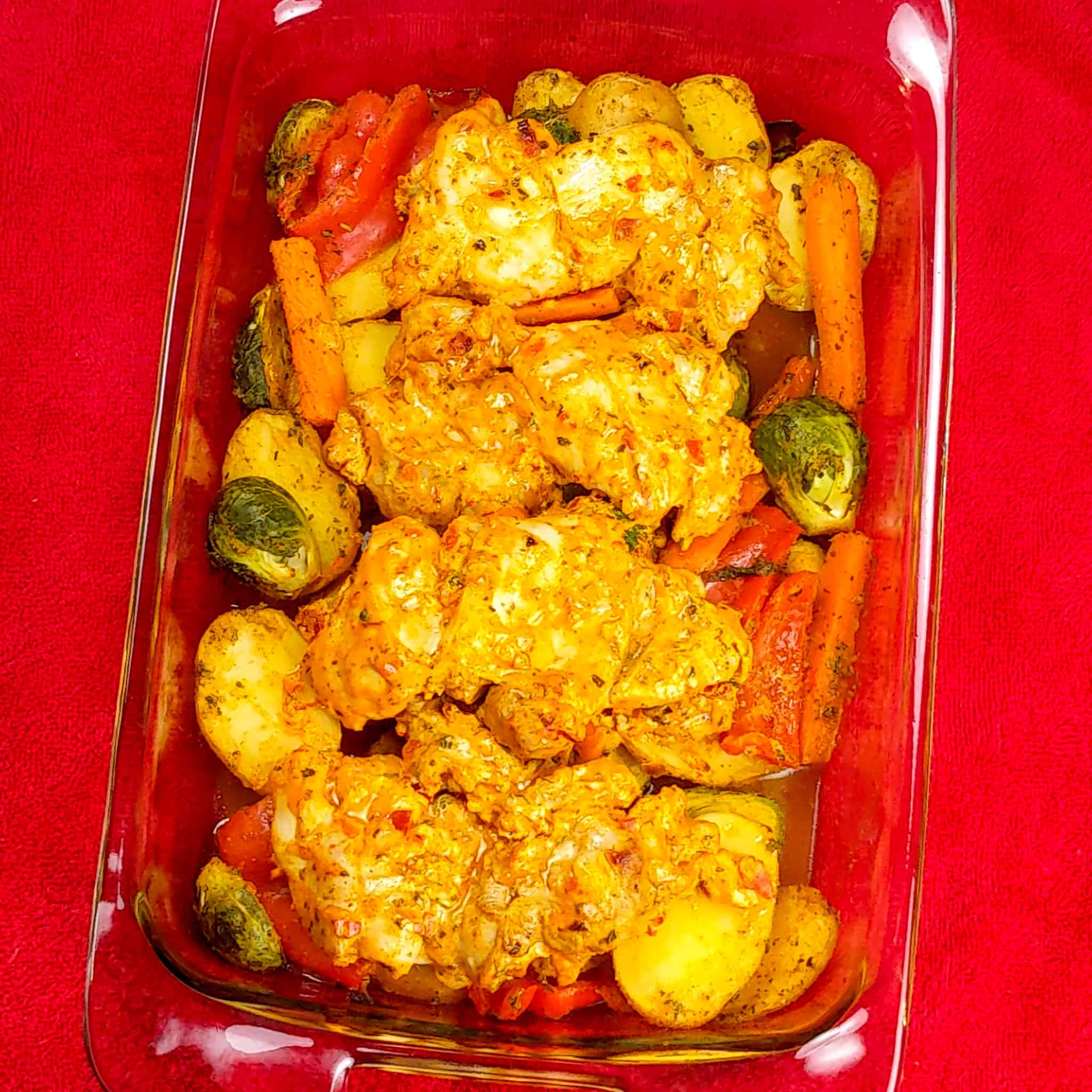 baked vegetables and yogurt chicken thighs in a rectangle glass baking dish for the Calabrian Pepper & Lemon Yogurt Baked Chicken and Vegetables recipe on a kitchen towel.