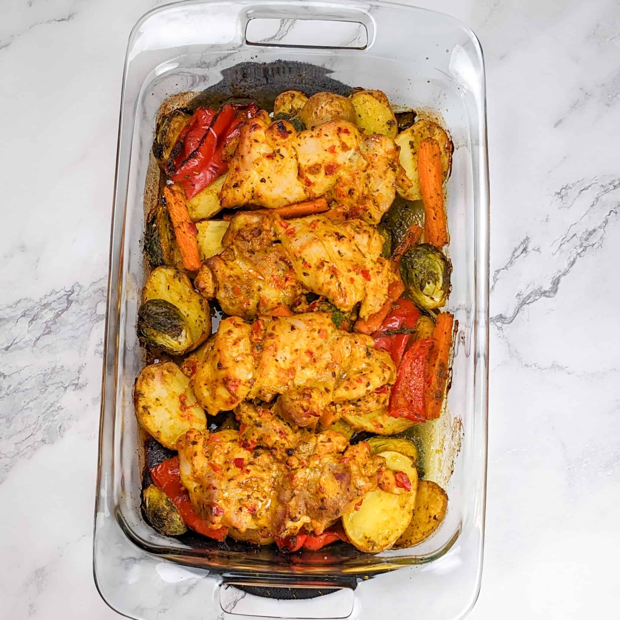 baked vegetables and yogurt chicken thighs in a rectangle glass baking dish for the Calabrian Pepper & Lemon Yogurt Baked Chicken and Vegetables recipe on the counter