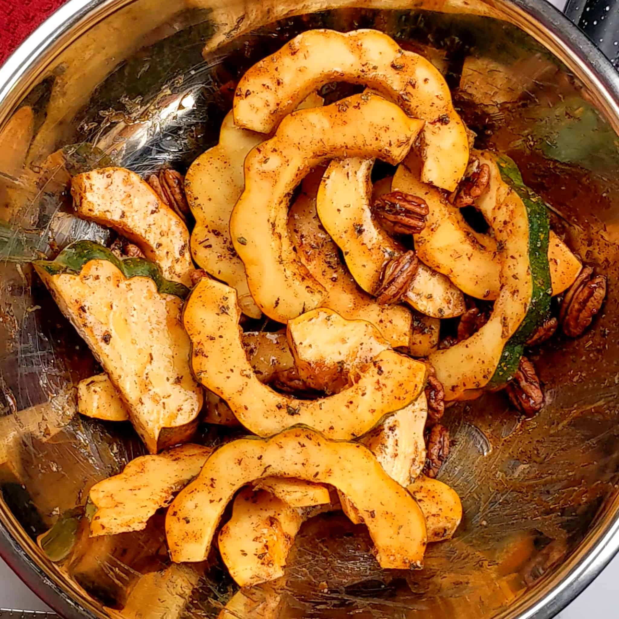 seasoned sliced acorn squash and whole pecans in a large mixing bowl