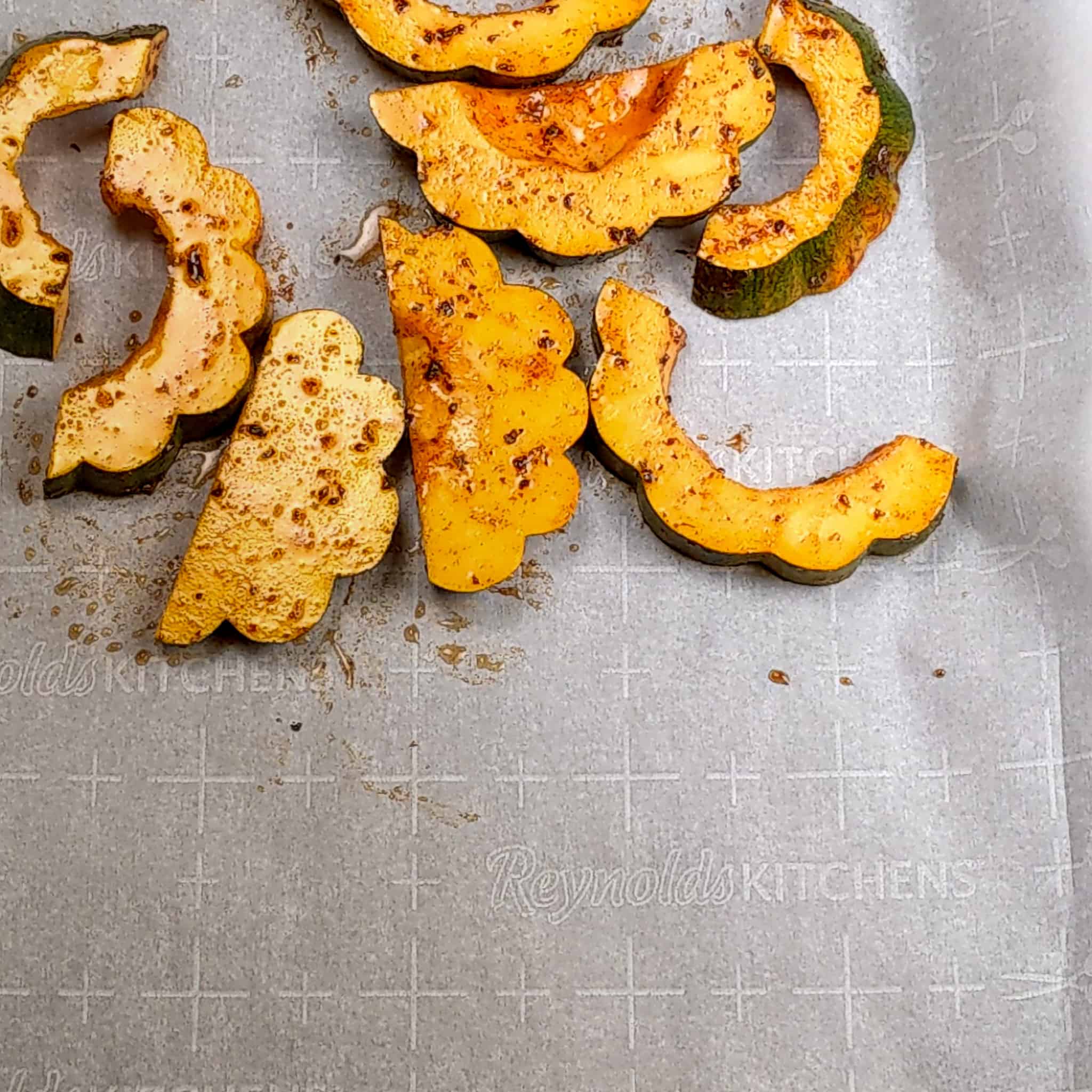 seasoned acorn squash on one side of a sheet pan lined with parchment paper for the chicken paillard salad