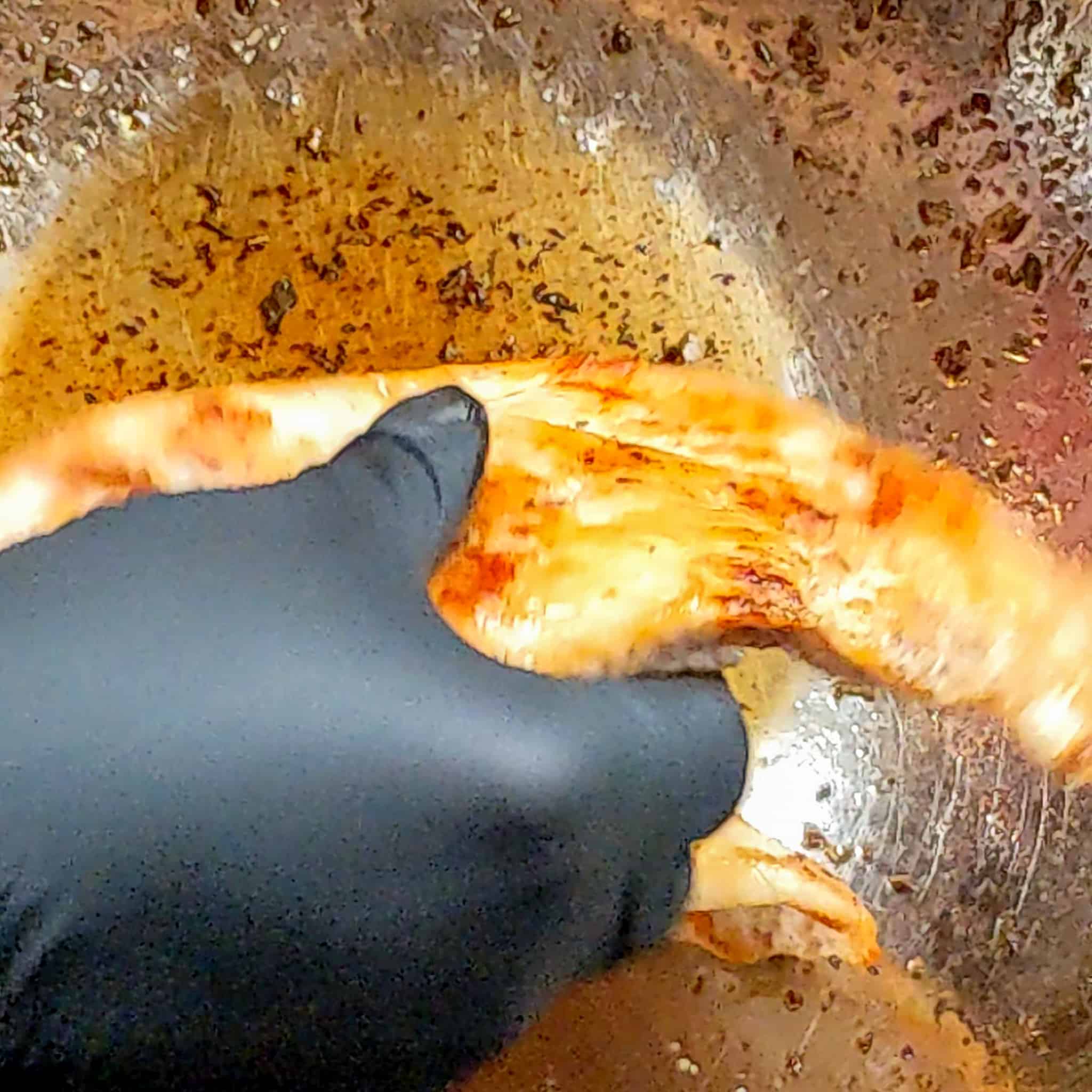 a gloved hand about to place a seared cooked seasoned chicken breast in a large mixing bowl of maple syrup sauce