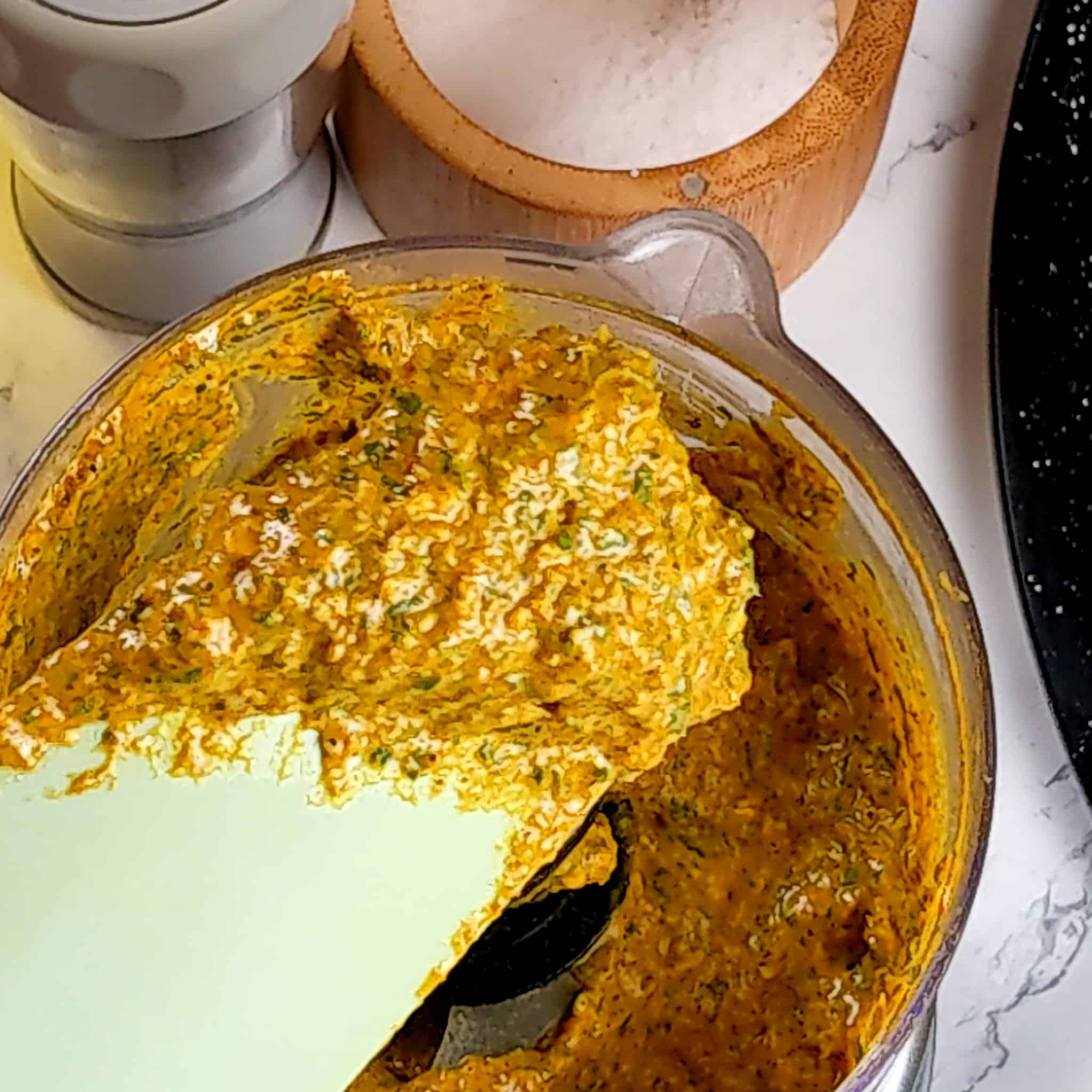 the prepared curry wet rub paste in a food process and on top of the silicone spatula being held above the food process.