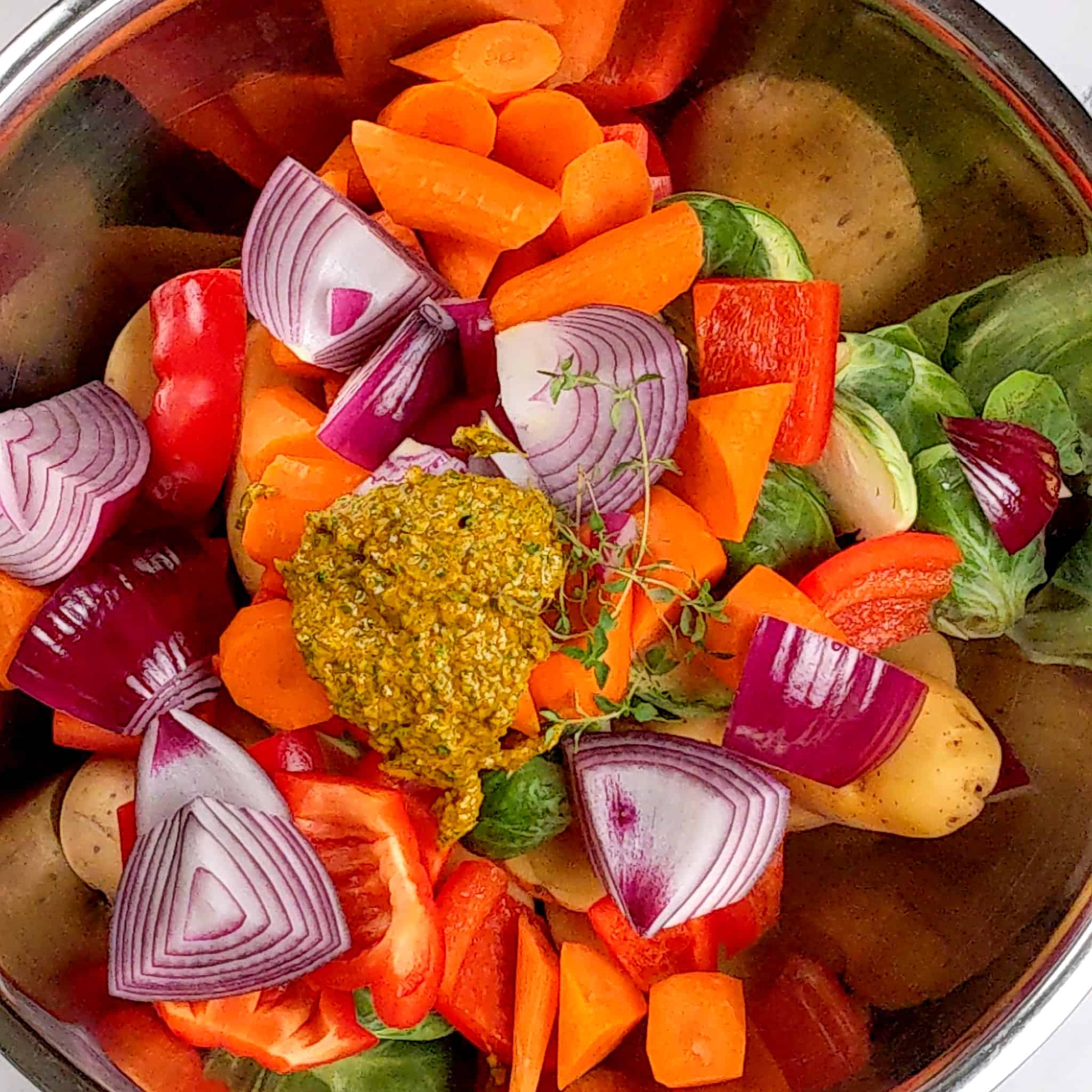 the wet rub paste on top of a large stainless steel bowl of mixed cut vegetables