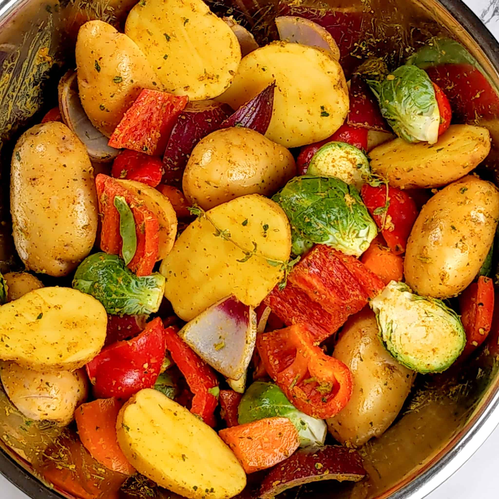 a large metal mixing bowl with seasoned cut vegetables for the roast curry spatchcocked chicken and vegetables recipe.