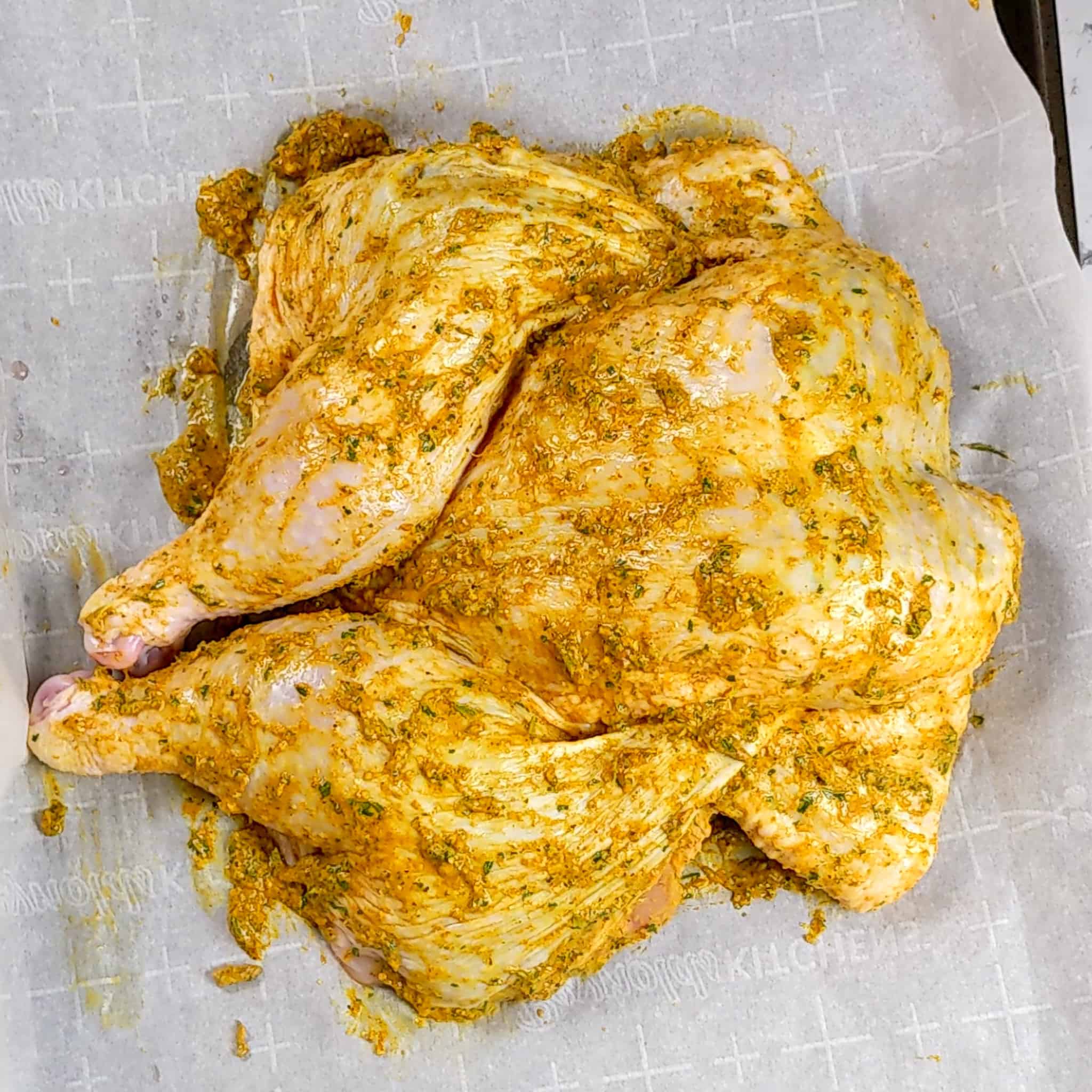 wet rub seasoned spatchcocked chicken with wings tucked in a on parchment paper layered sheet pan