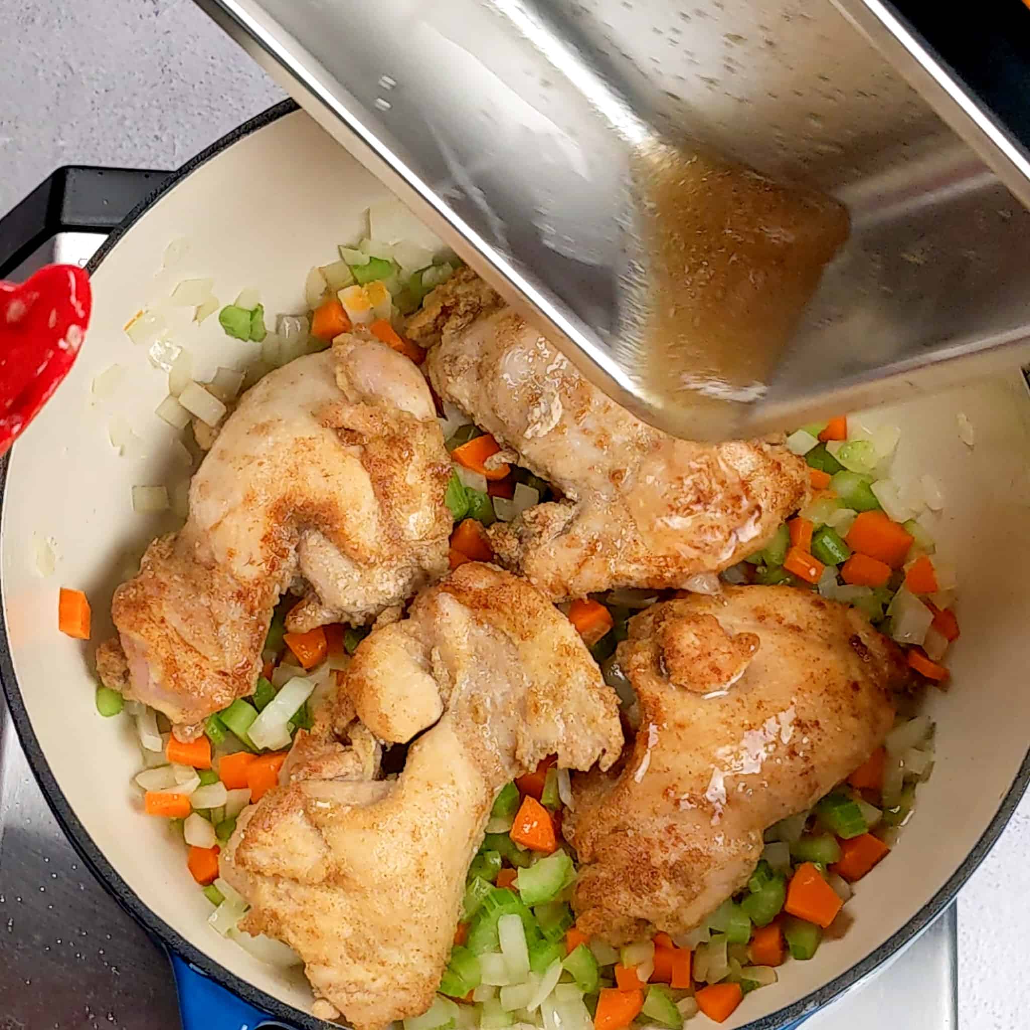 golden brown chicken thighs on top of carrots, onions and celery in a Dutch oven with a small rectangular tray above it pour the chicken juices into the pot