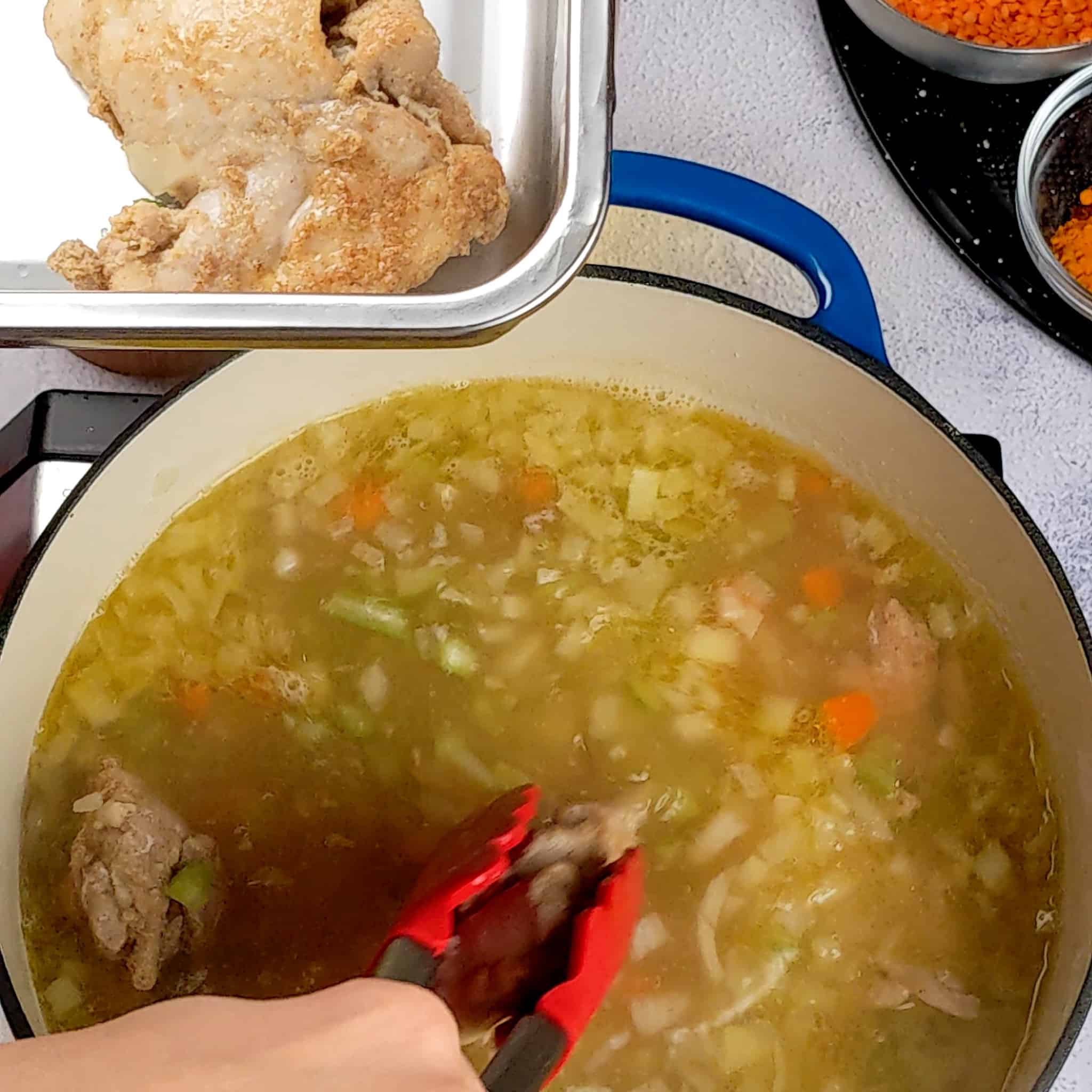 cooked thighs being removed form the dutch oven and placed in a deep rectangular metal container.