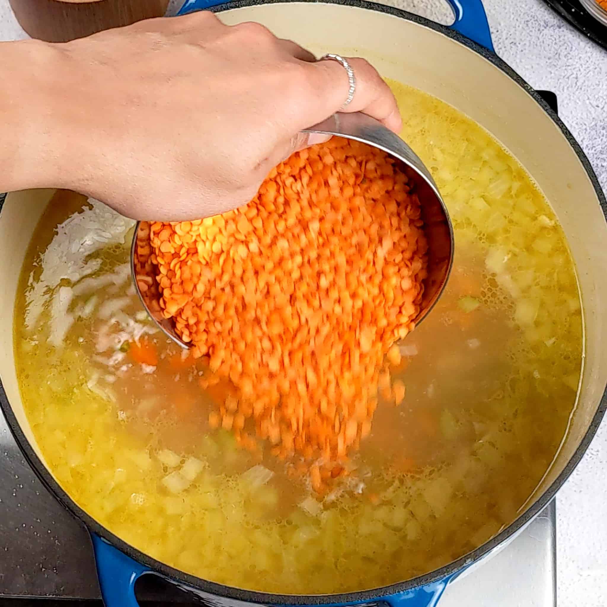 split red lentils in a bowl being poured into the chicken broth of seasoned vegetables