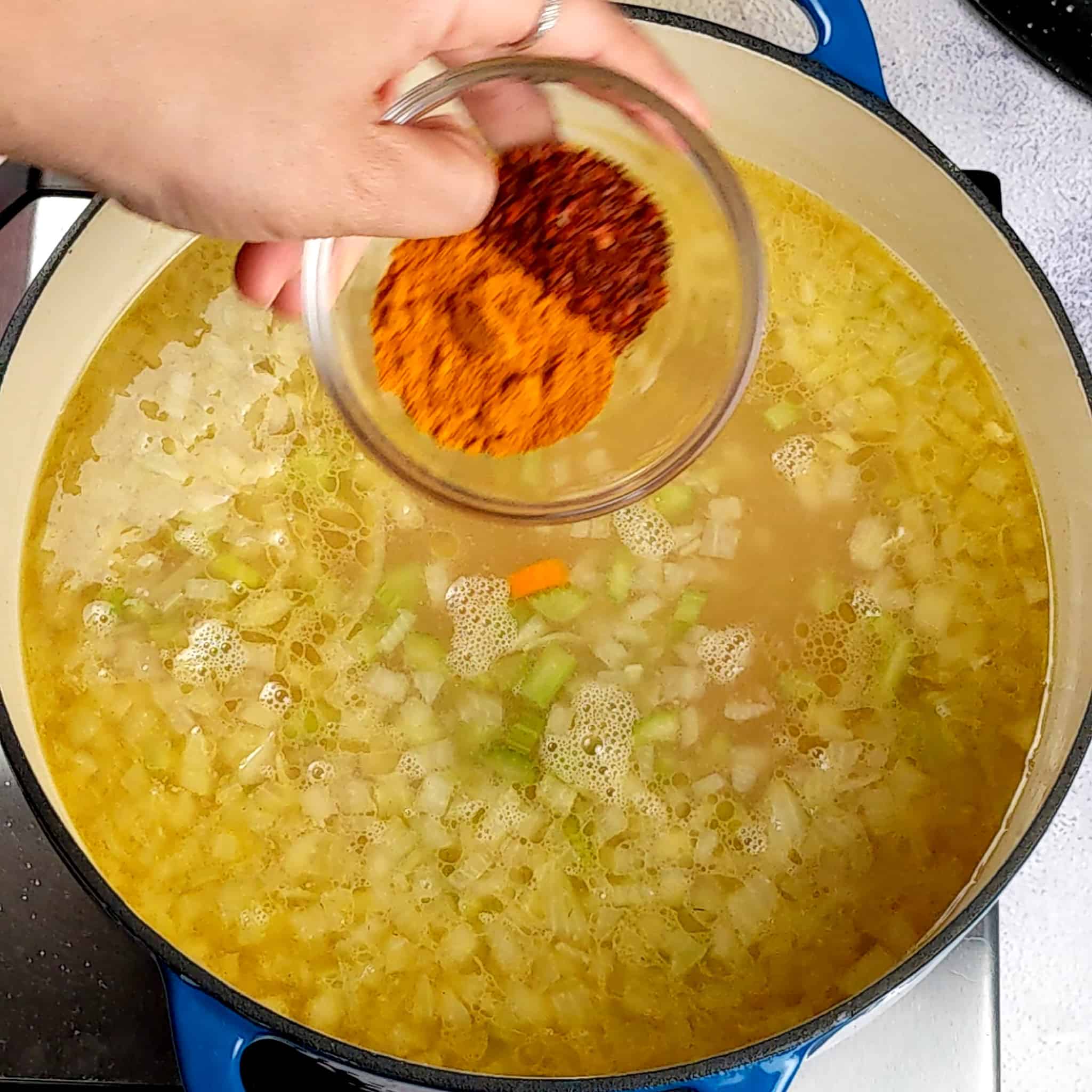 a small g glass bowl of turmeric and aleppo peppers about to be dropped into a pot of simmering broth