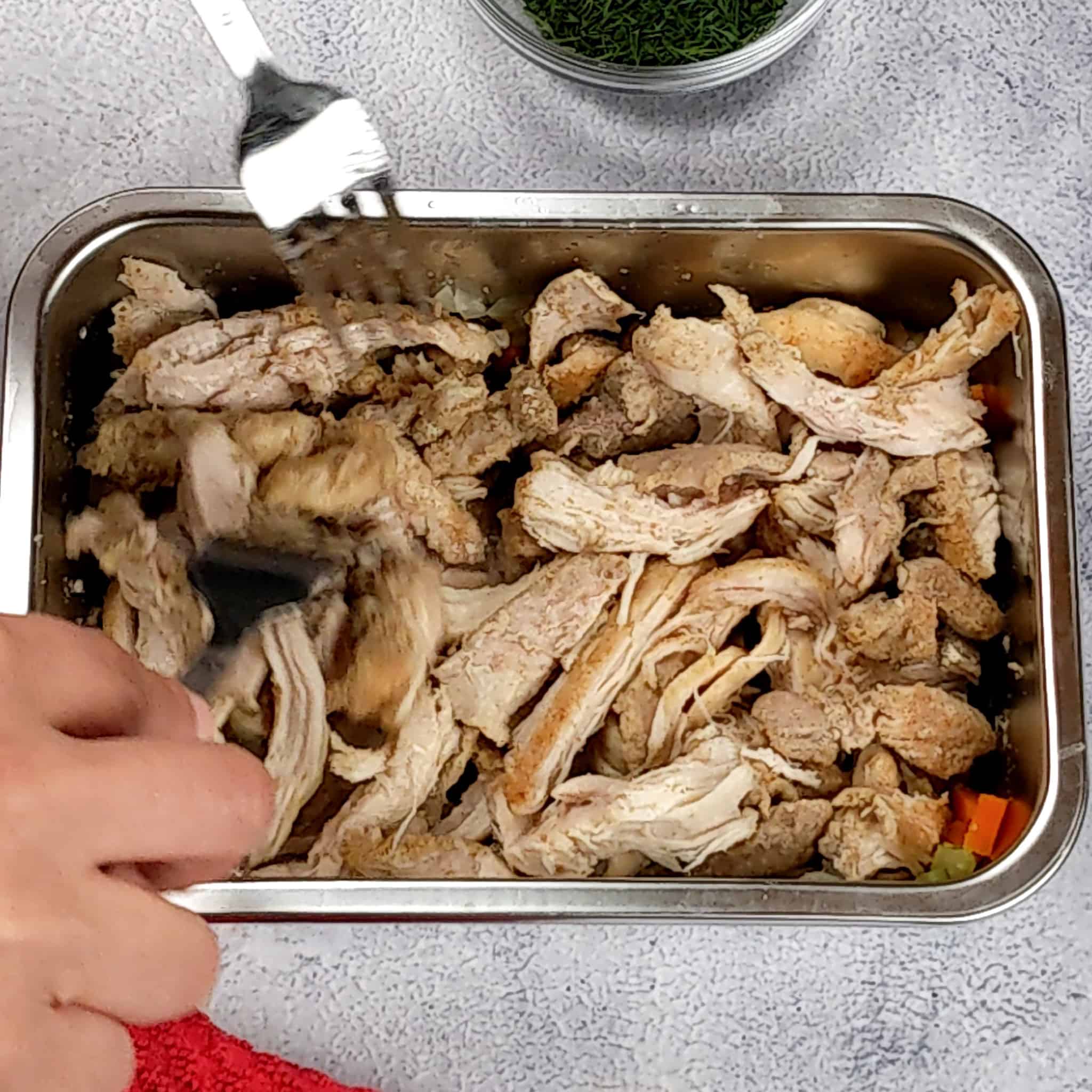 cooked chicken thighs being shredded with a pair of forks in a rectangular small metal container