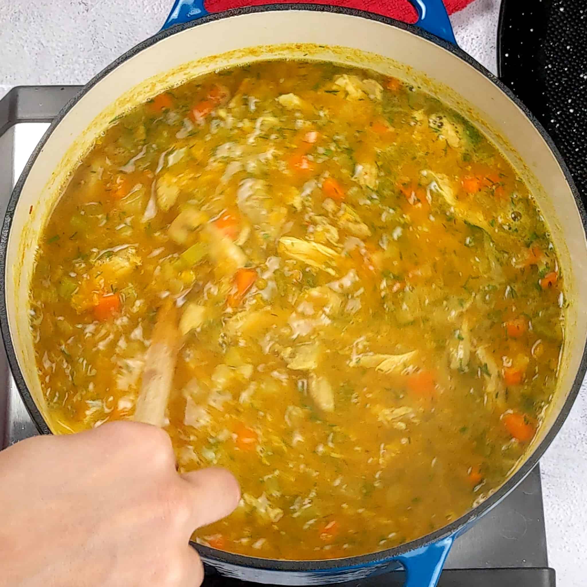 a wooden spoon is being used to stir the dill lentil chicken soup