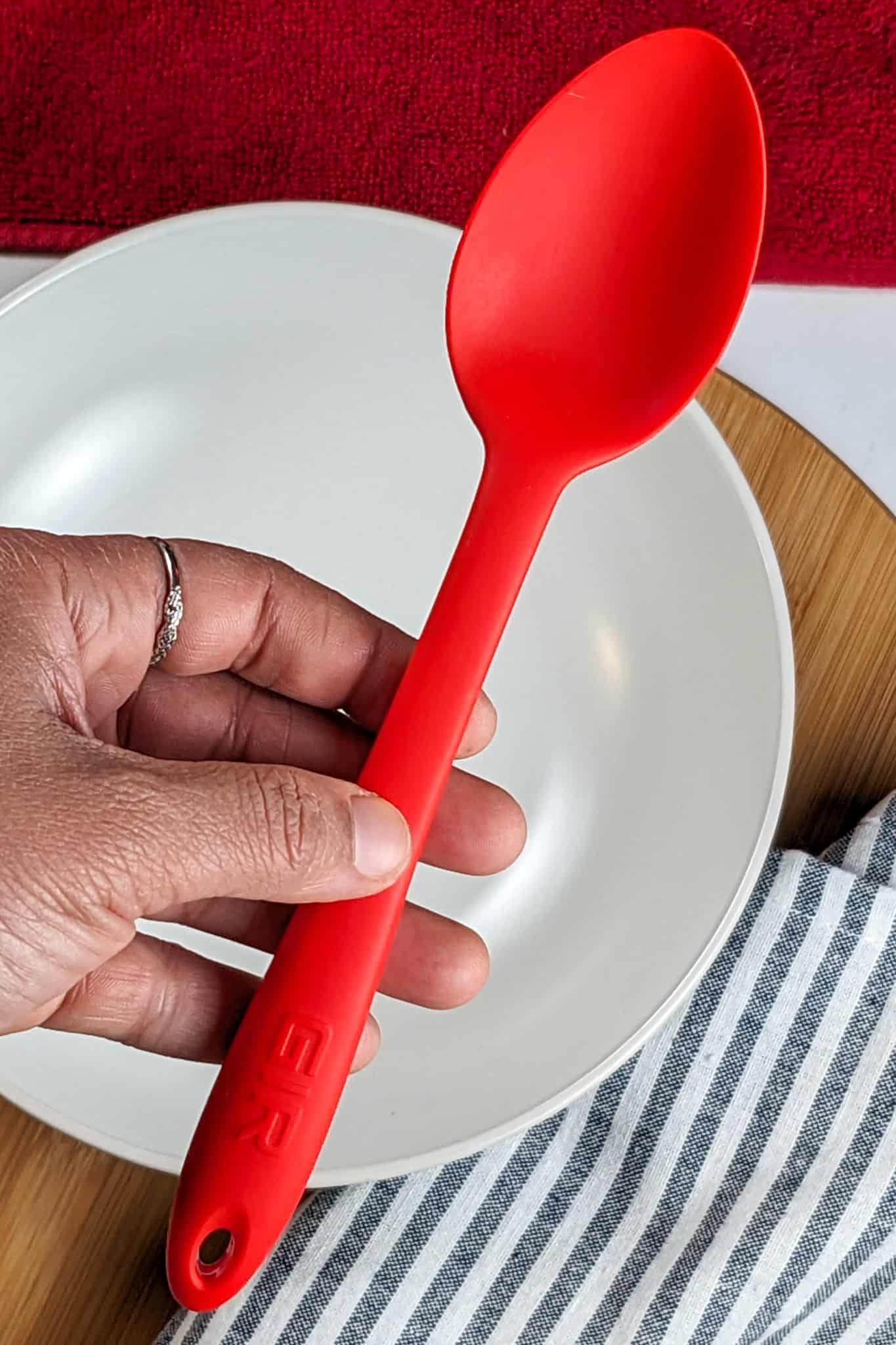 GIR: Get It Right premium silicon heat-resistant kitchen spoon held in the hand over a bowl, and kitchen towels in the background.