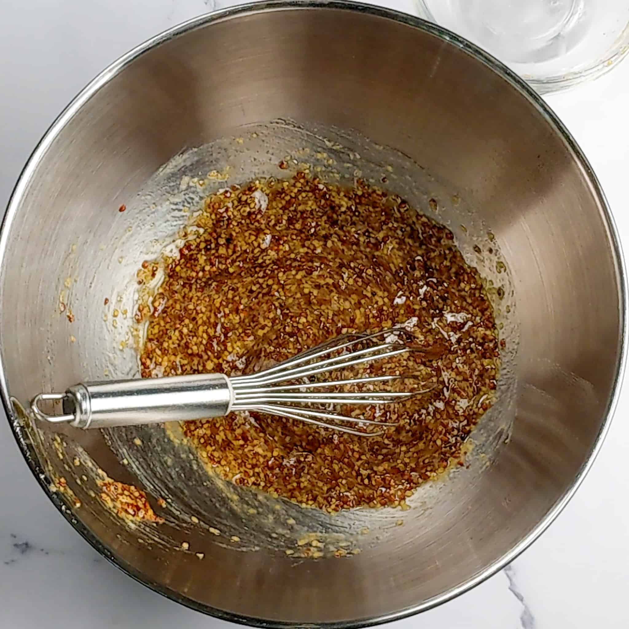 a bowl with honey and whole grain Dijon mustard combined with a whisk which is laying int he stainless steel bowl.