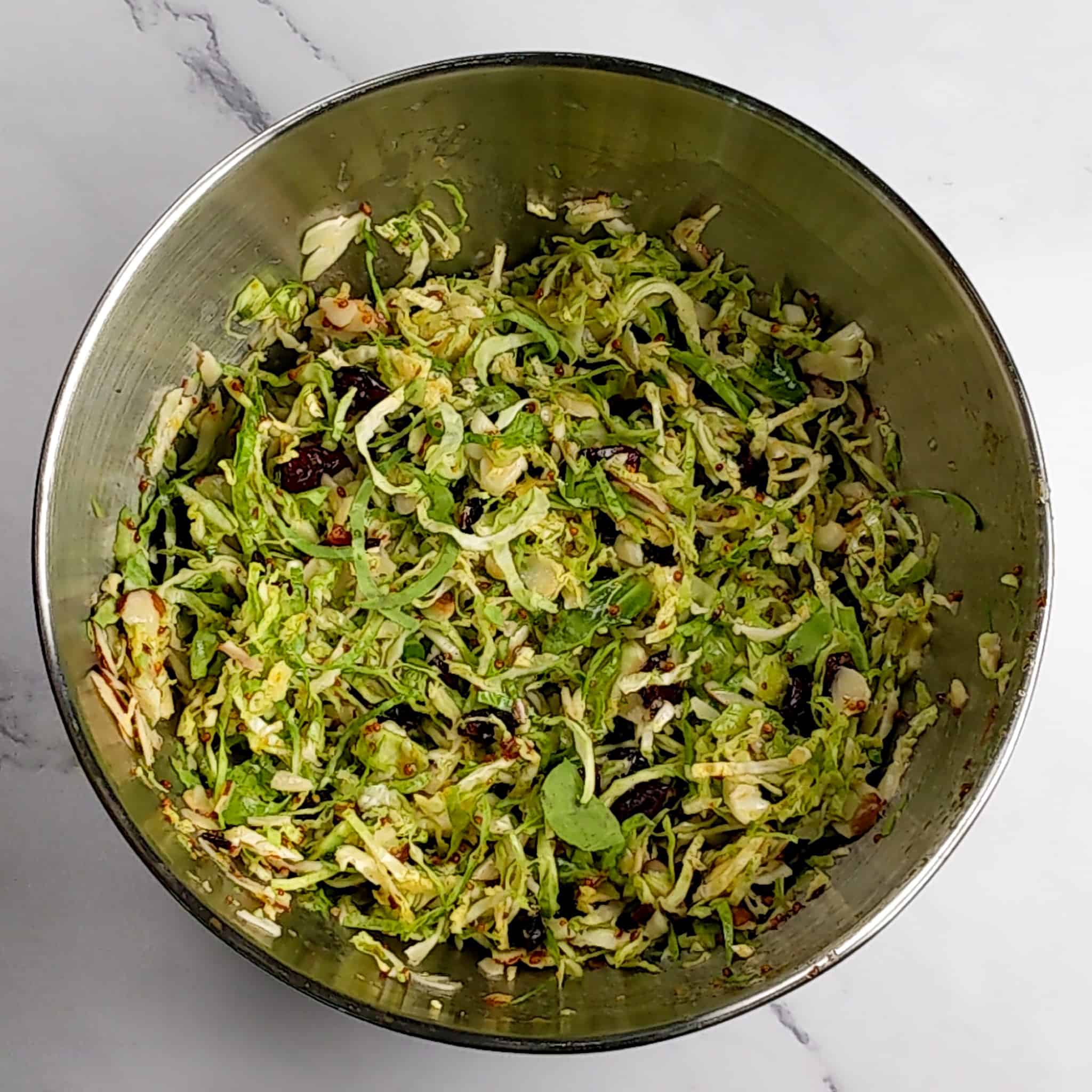 shaved brussels sprout salad tossed in a stainless steel mixing bowl for the Honey Dijon Chicken Rice Bowl
