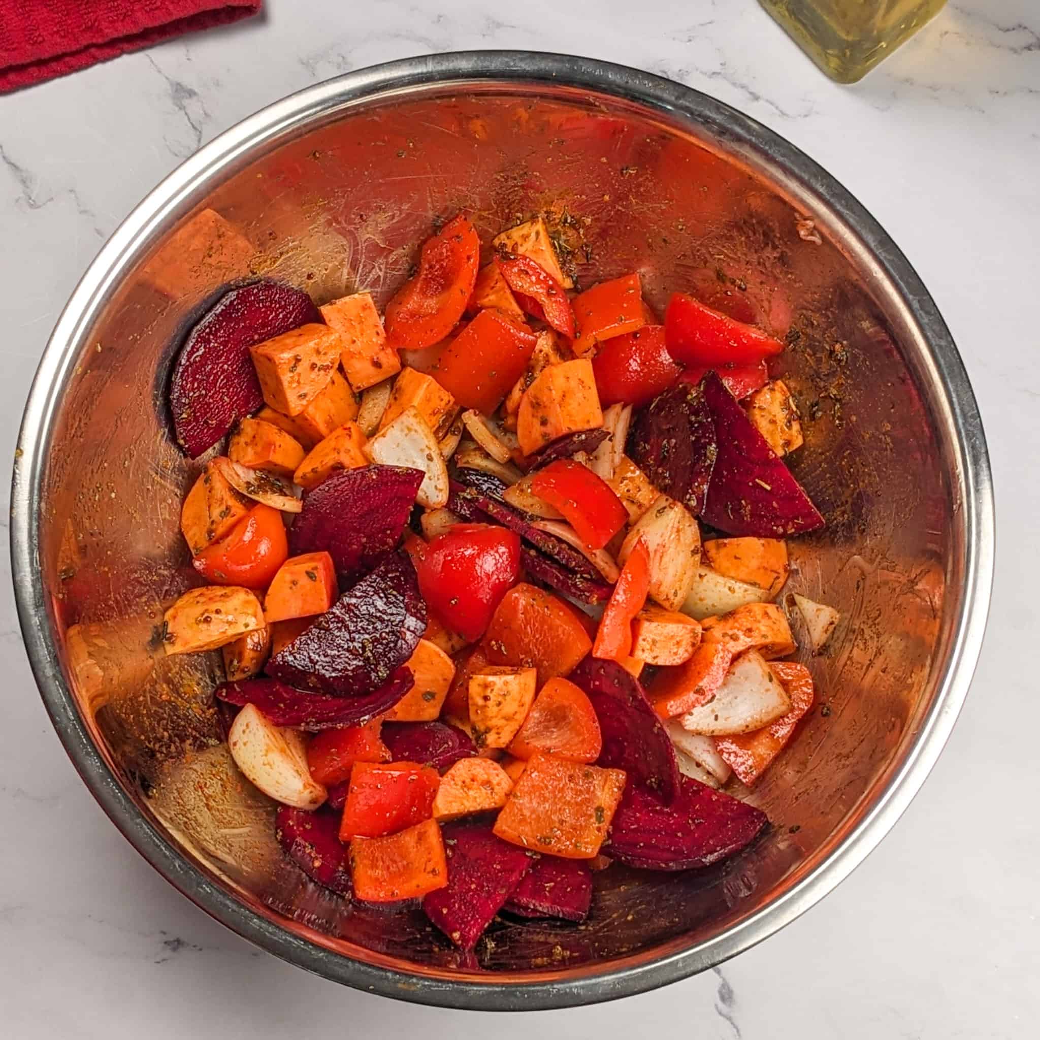 seasoned and tossed mixed root vegetable and onion in a large wide stainless steel mixing bowl.