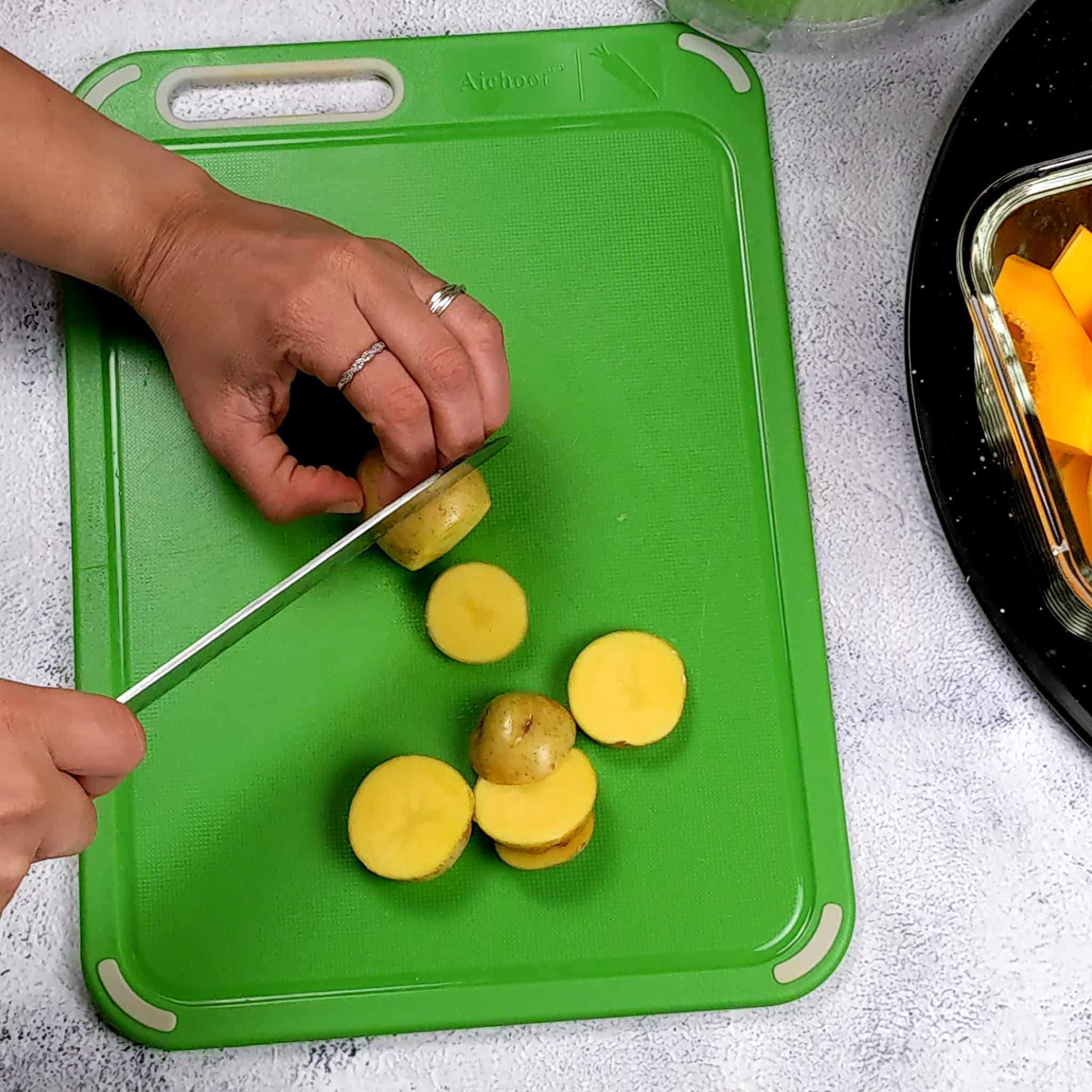 a baby Dutch yellow potato being cut into thick slices on a small color coded cutting board with a knife