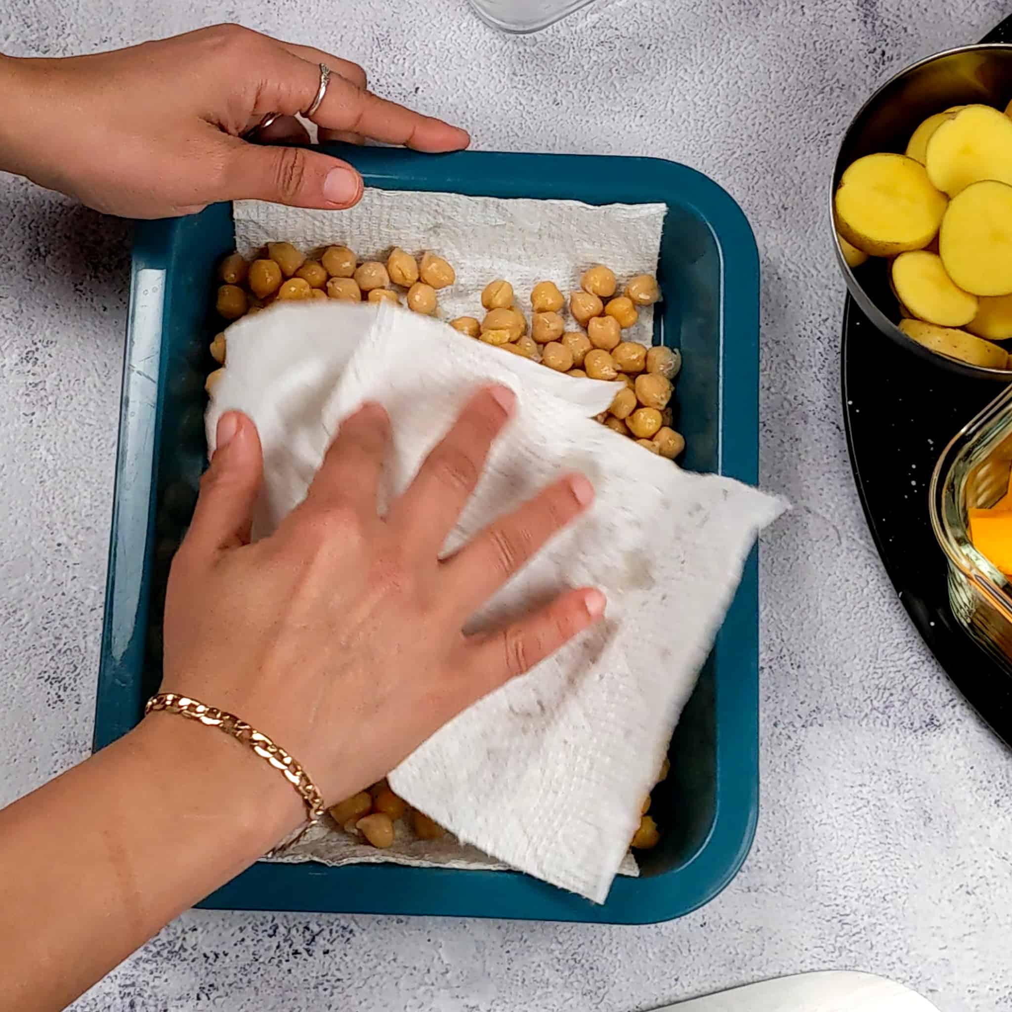 chickpeas sitting on a paper towel in a rectangular plastic container being dried off with a paper towel