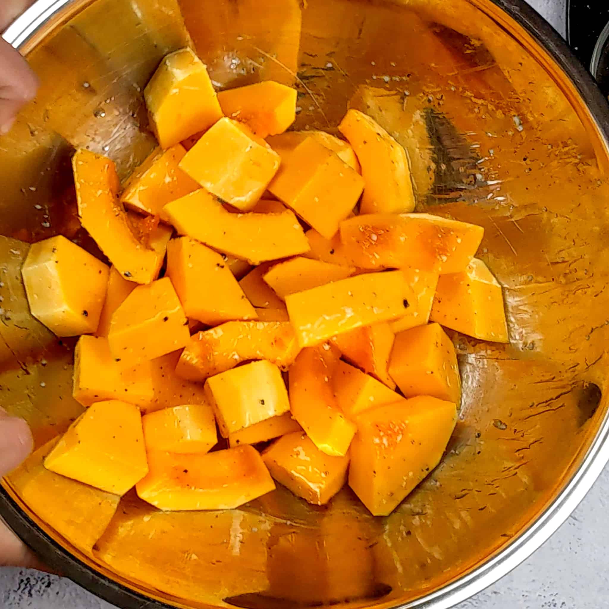 thick sliced butternut squash tossed in avocado oil, salt and pepper in a large stainless steel mixing bowl