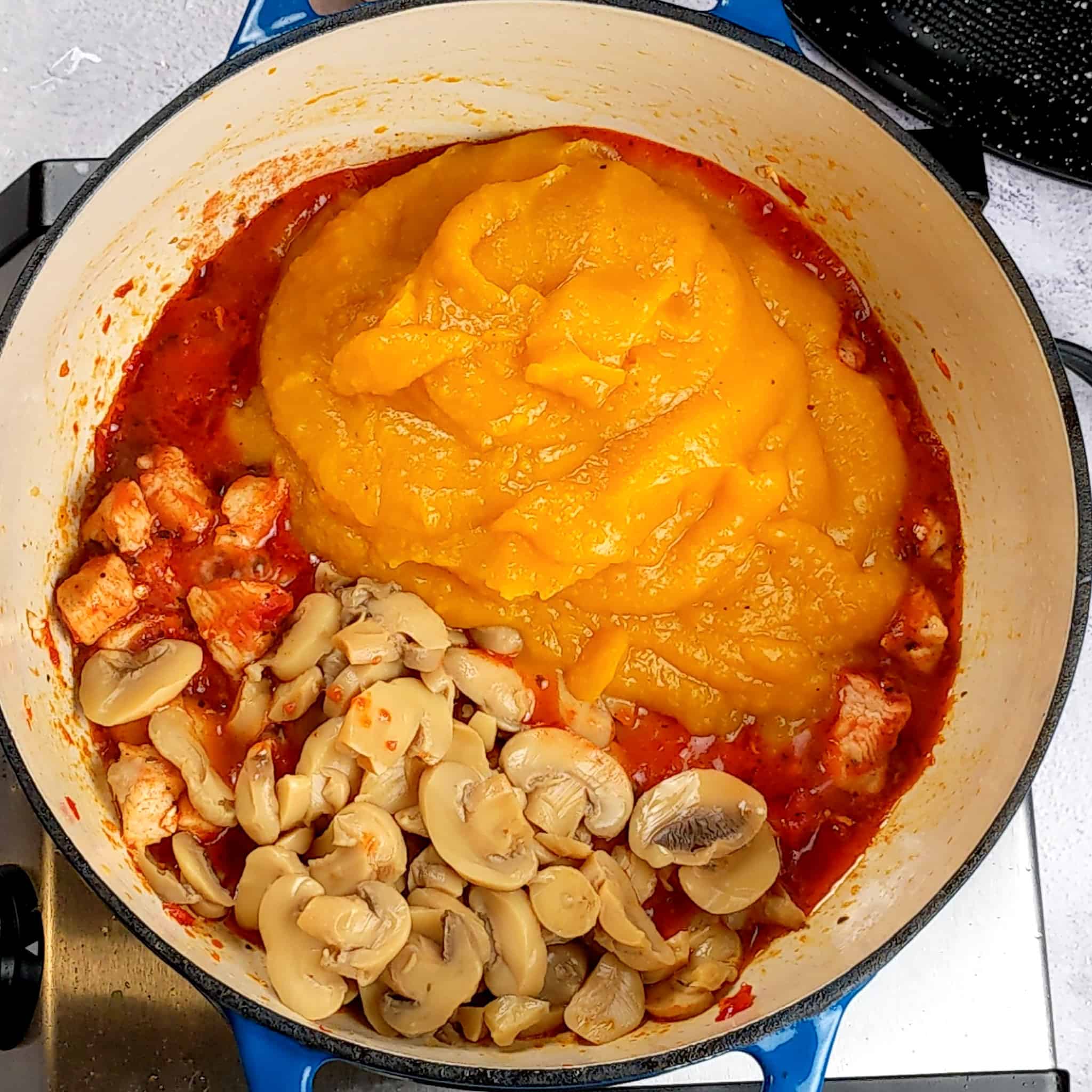 Dutch oven with diced cooked chicken submerged in crushed calabrian peppers and crushed fire roasted tomatoes, topped with puree roasted butternut squash and sliced canned mushrooms.