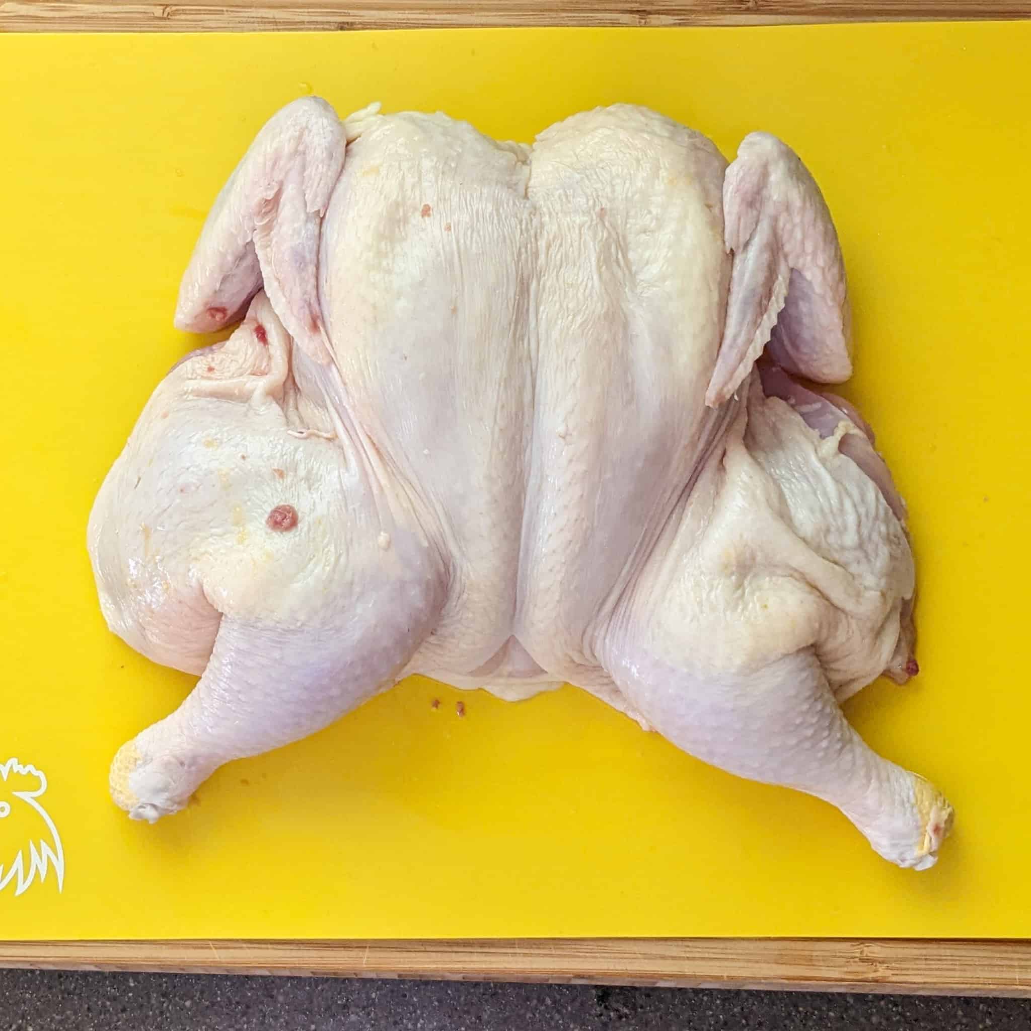 Finish product, a spatchcock chicken that has been flatten breast side up on a cutting board for poultry