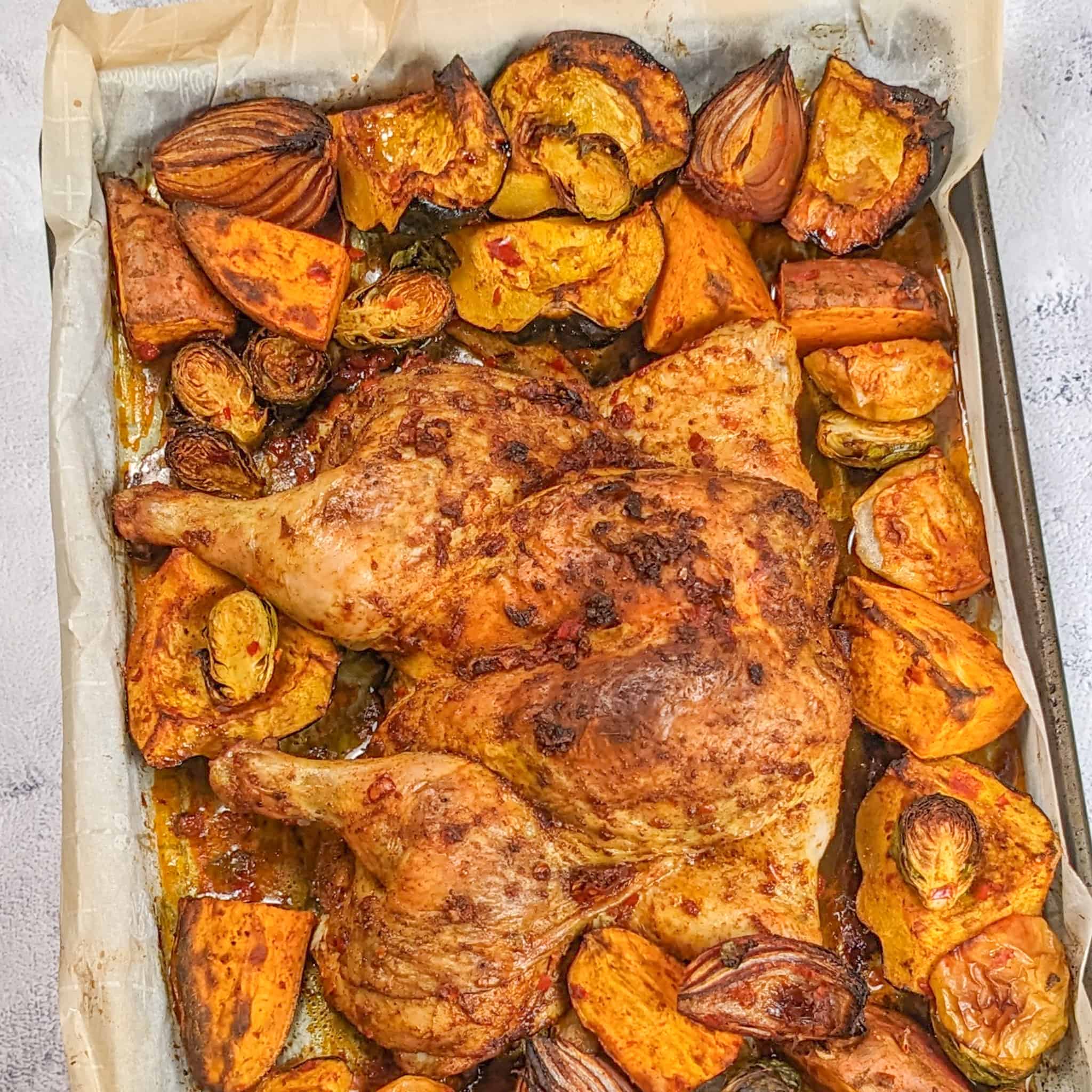 Roasted Calabrian Pepper Spatchcocked Chicken & Vegetables on a sheet pan with parchment paper